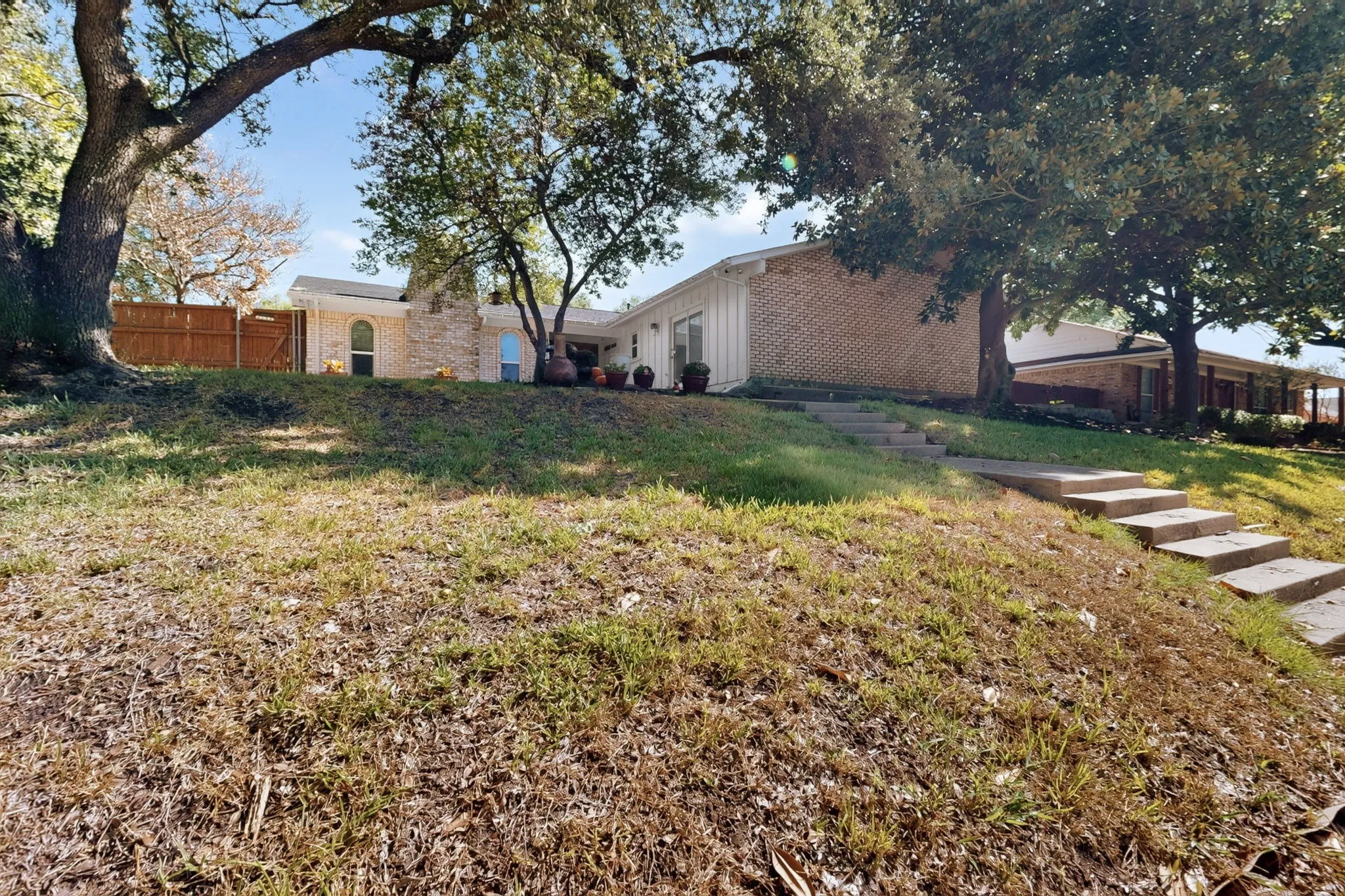 Brick exterior residence with a sloped front yard, concrete steps, and mature trees