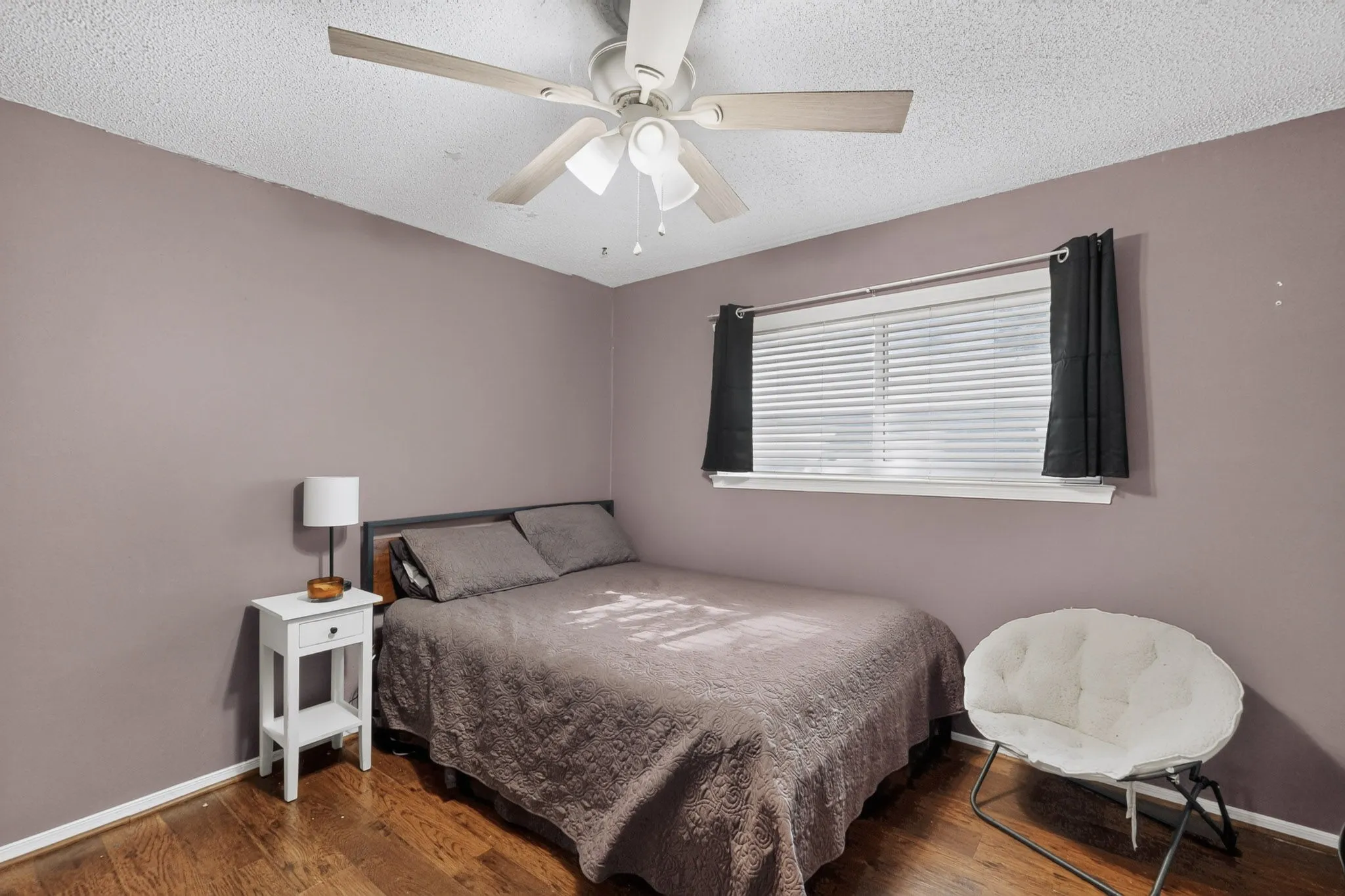Wood-finish flooring, ceiling fan with light fixture, window with blinds, and painted walls