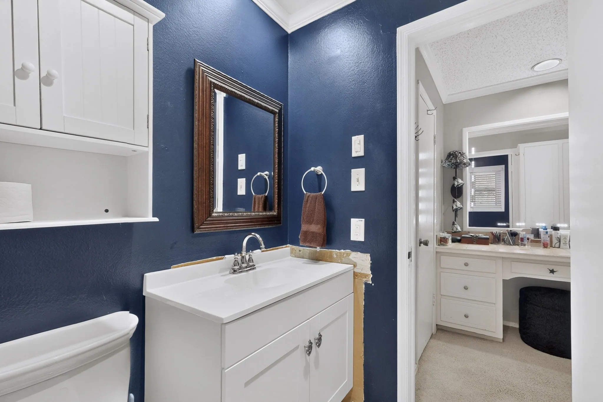 White vanity with a single basin sink, wall-mounted mirror, and white overhead cabinetry