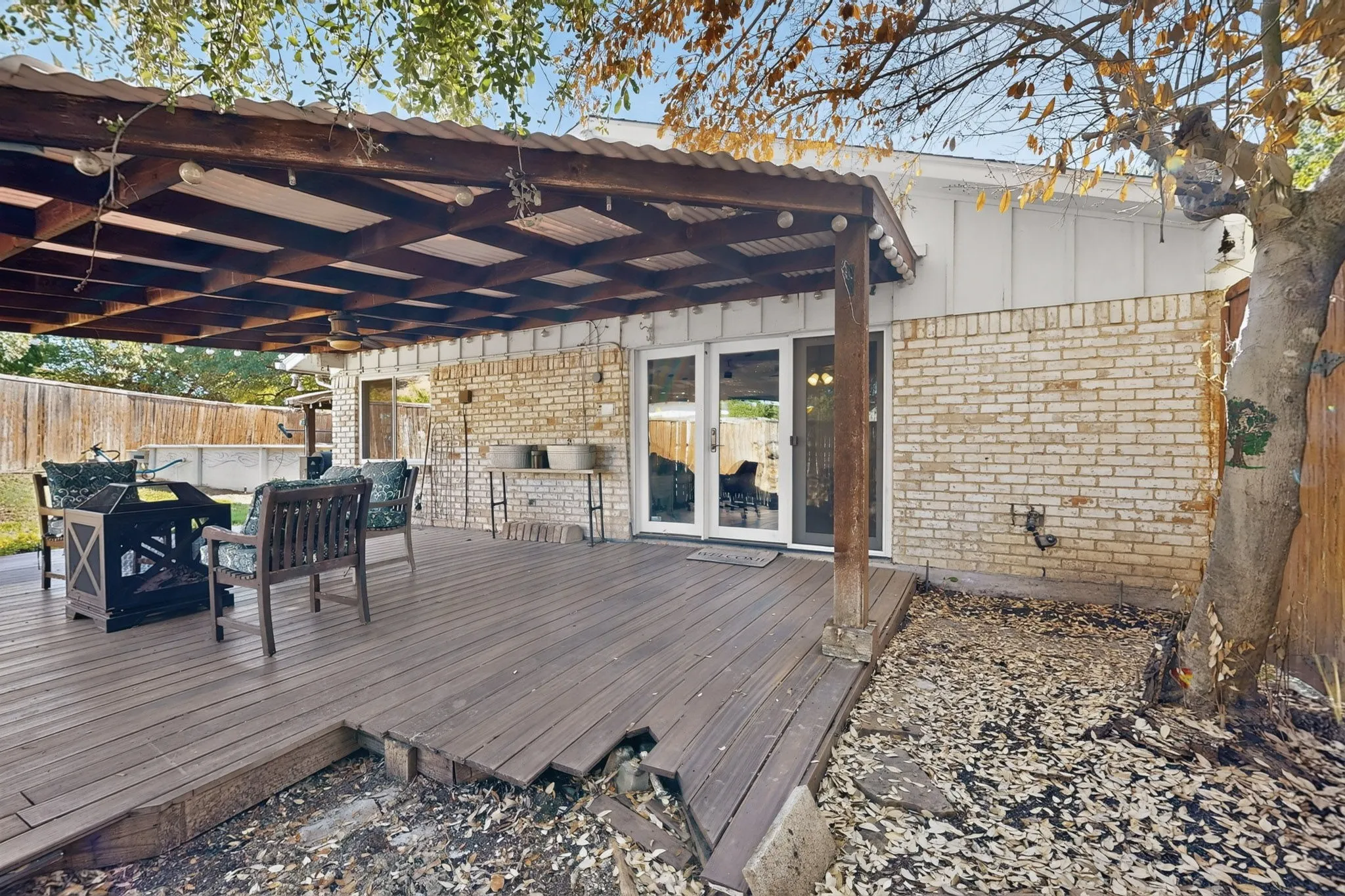 Expansive wood-finish deck with a substantial overhead pergola, dual sets of French doors, and a brick exterior