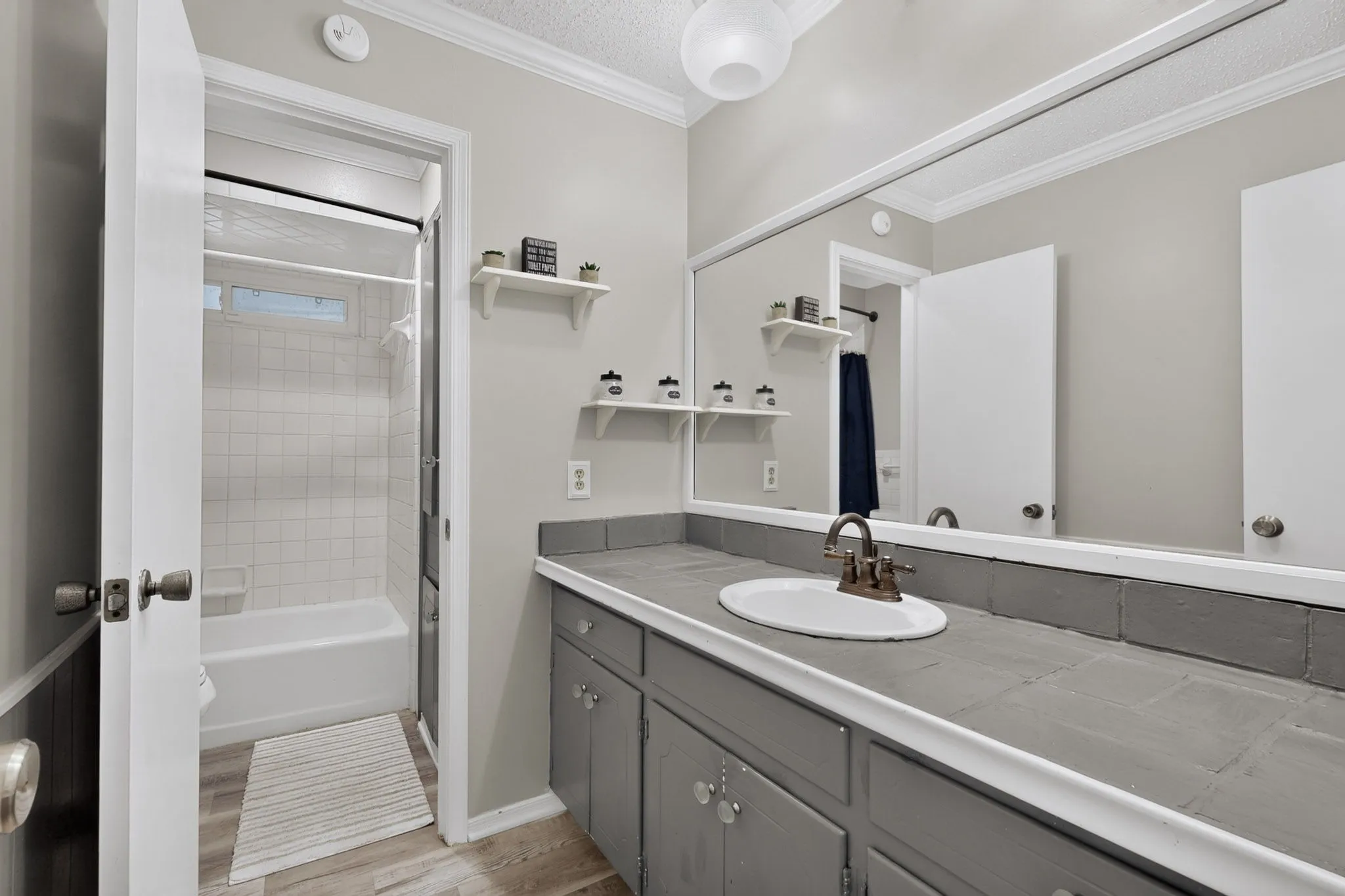 Vanity with an integrated sink and bronze-finish faucet, a full-width wall mirror, and wood-finish flooring