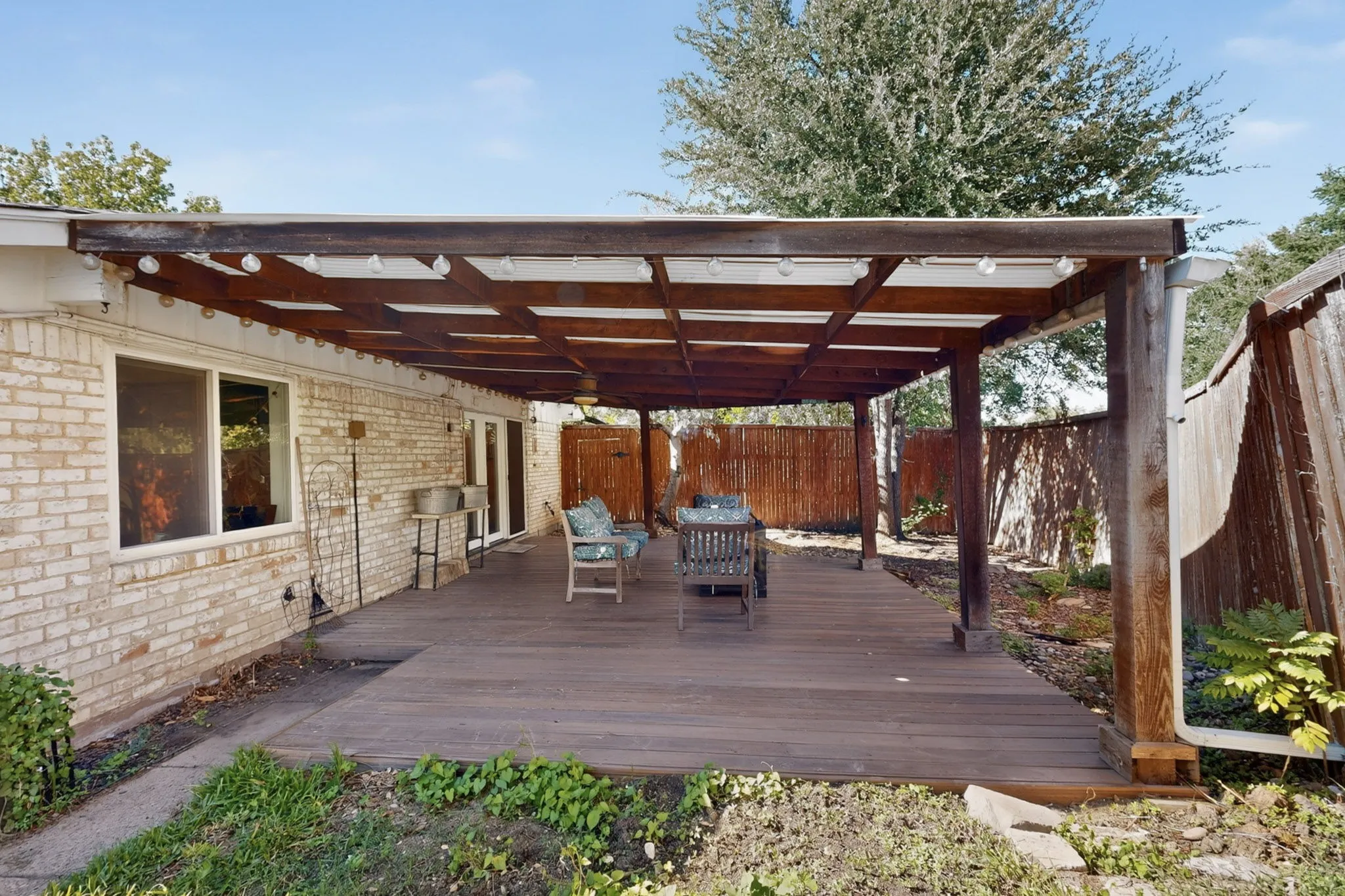 Expansive wood-finish deck with a substantial wooden pergola, supported by robust columns, featuring string lighting