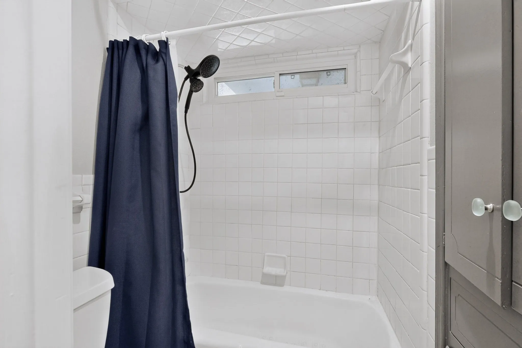 White subway tile shower surround with a built-in bathtub, a window, and an adjacent built-in cabinet