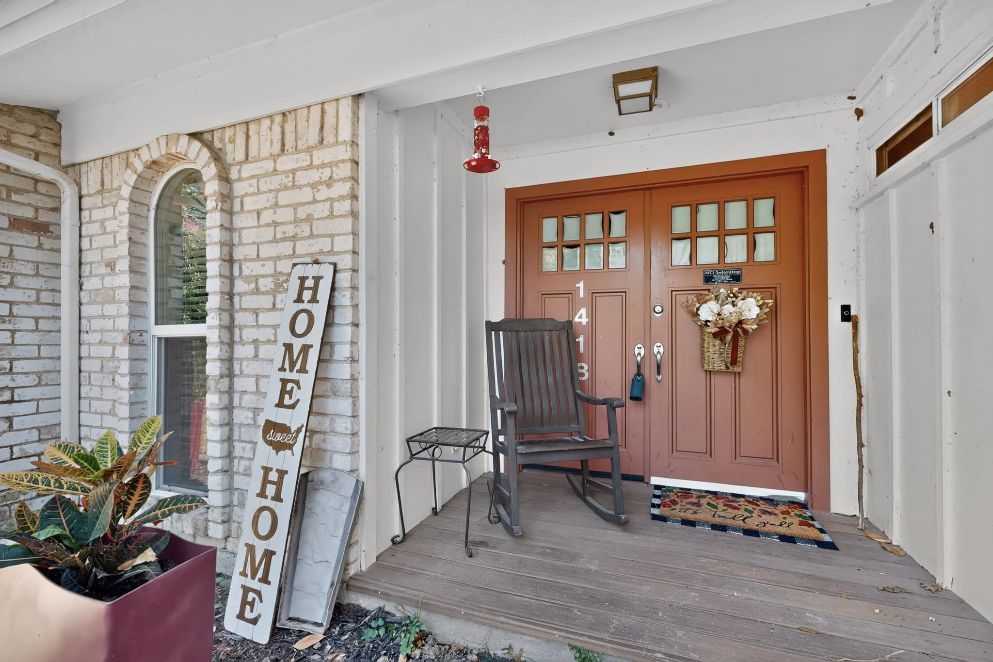 Front entry featuring a double door with glass-paneled inserts, white brick facade, arched window, and a covered porch