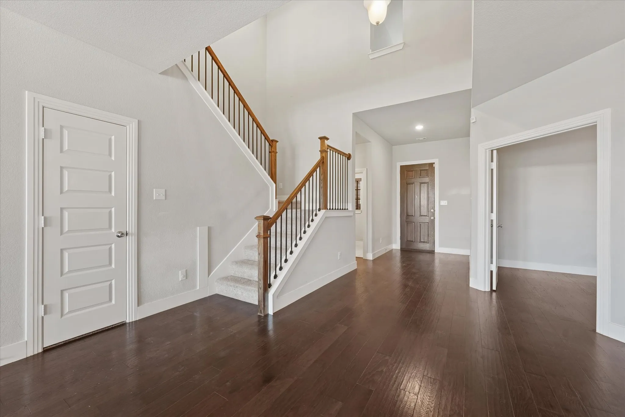 Two-story foyer featuring wood-finish flooring, a carpeted staircase with wood handrails and wrought iron balusters, and recessed lighting