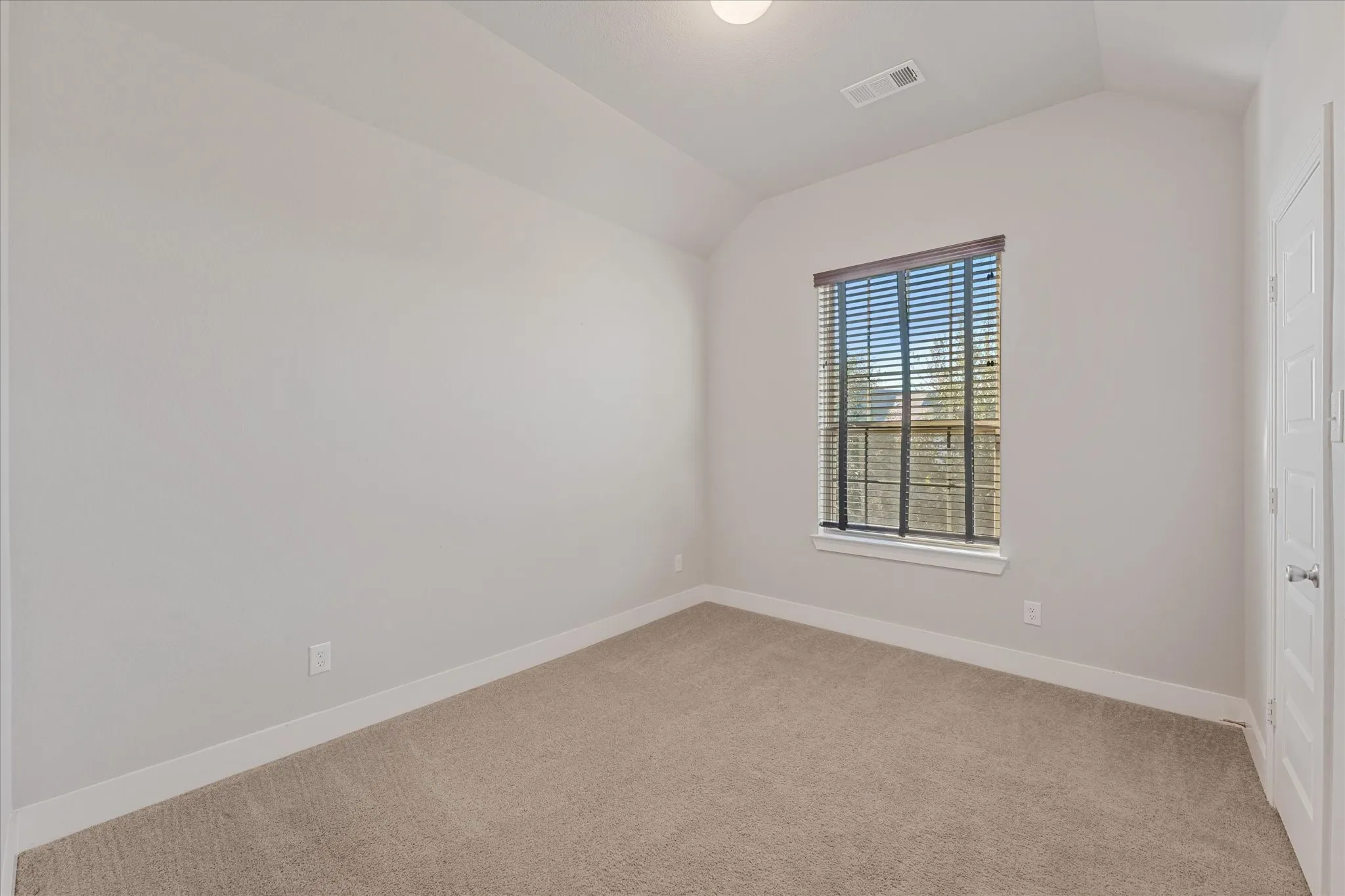 Carpeted flooring, vaulted ceiling, single window with blinds, recessed lighting, and a paneled door