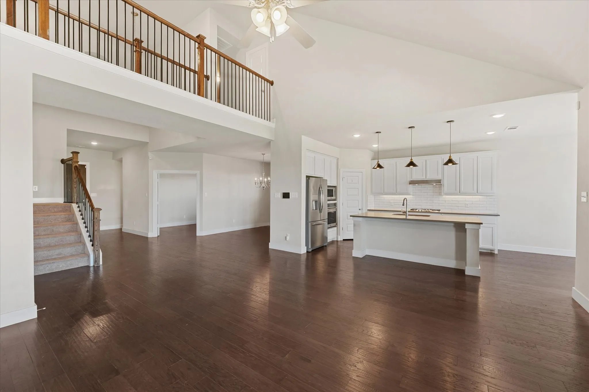 Open-concept living area featuring rich wood-finish flooring, a two-story ceiling, and a modern kitchen with a central island and pendant lighting
