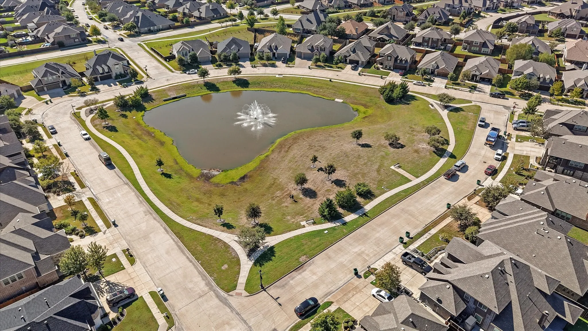 Centrally located pond with a water feature, surrounded by paved walkways, and mature trees