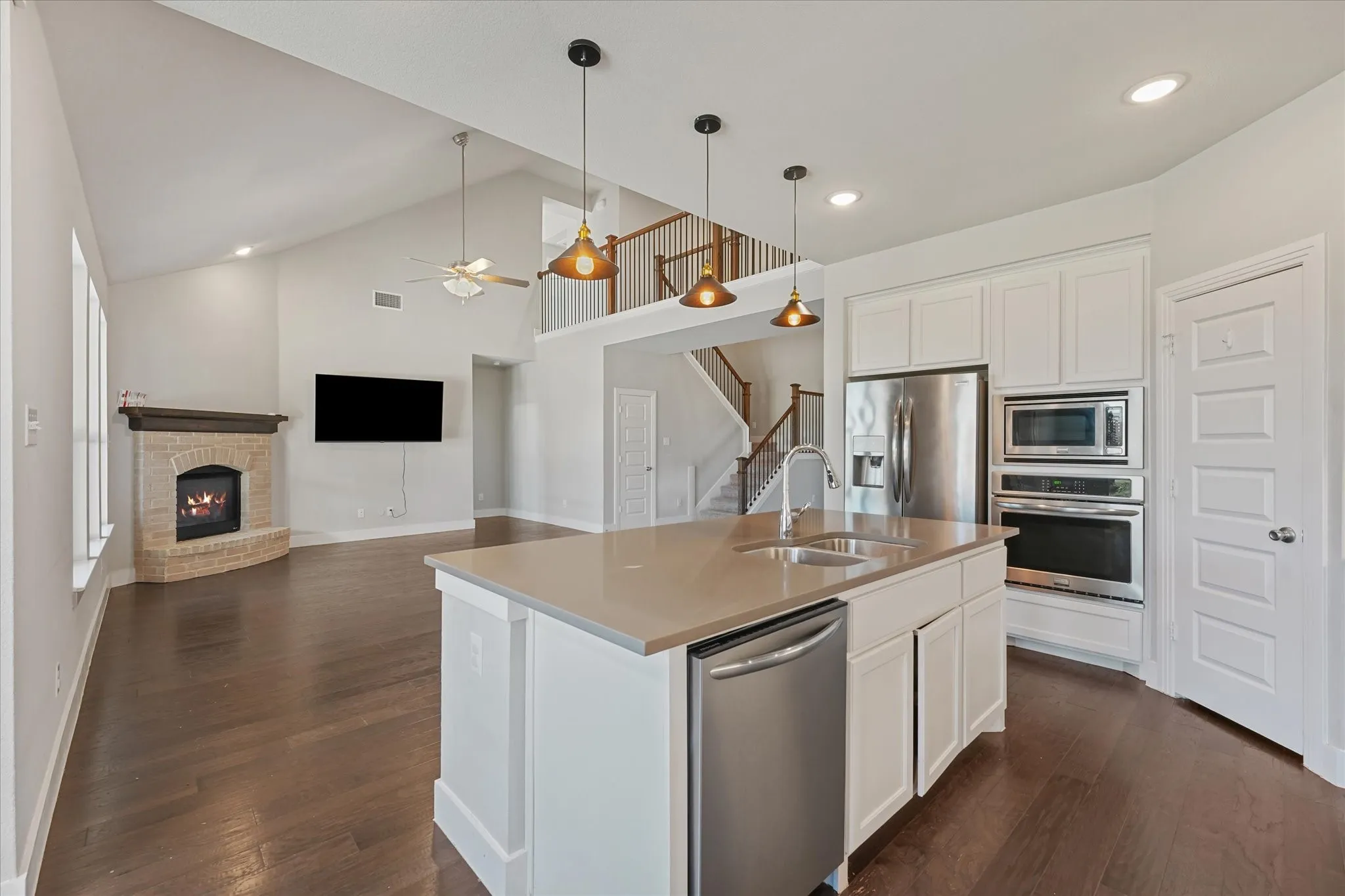 Open-concept living space with vaulted ceilings, a stone-clad fireplace, and wood-finish flooring