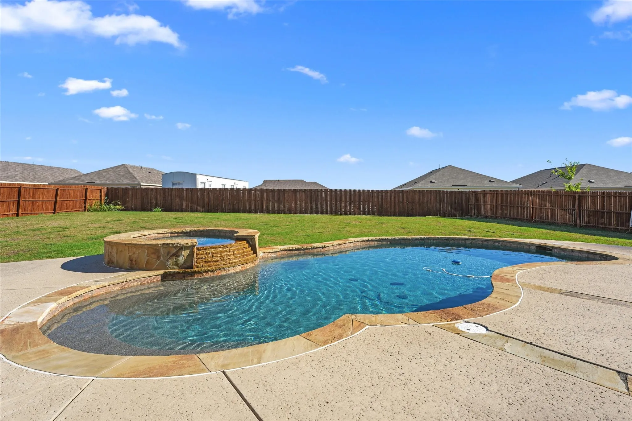 Inviting backyard featuring a freeform swimming pool, integrated spa with stone surround, perimeter concrete decking, and a privacy fence