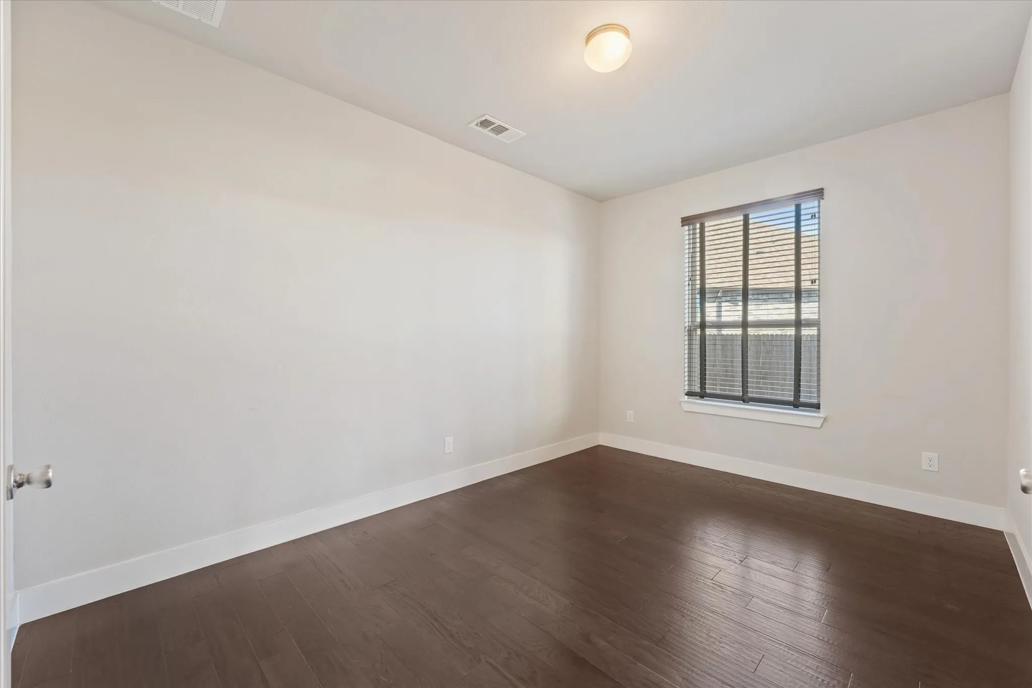Room with wood-finish flooring, a window with blinds, and a flush-mount ceiling light fixture