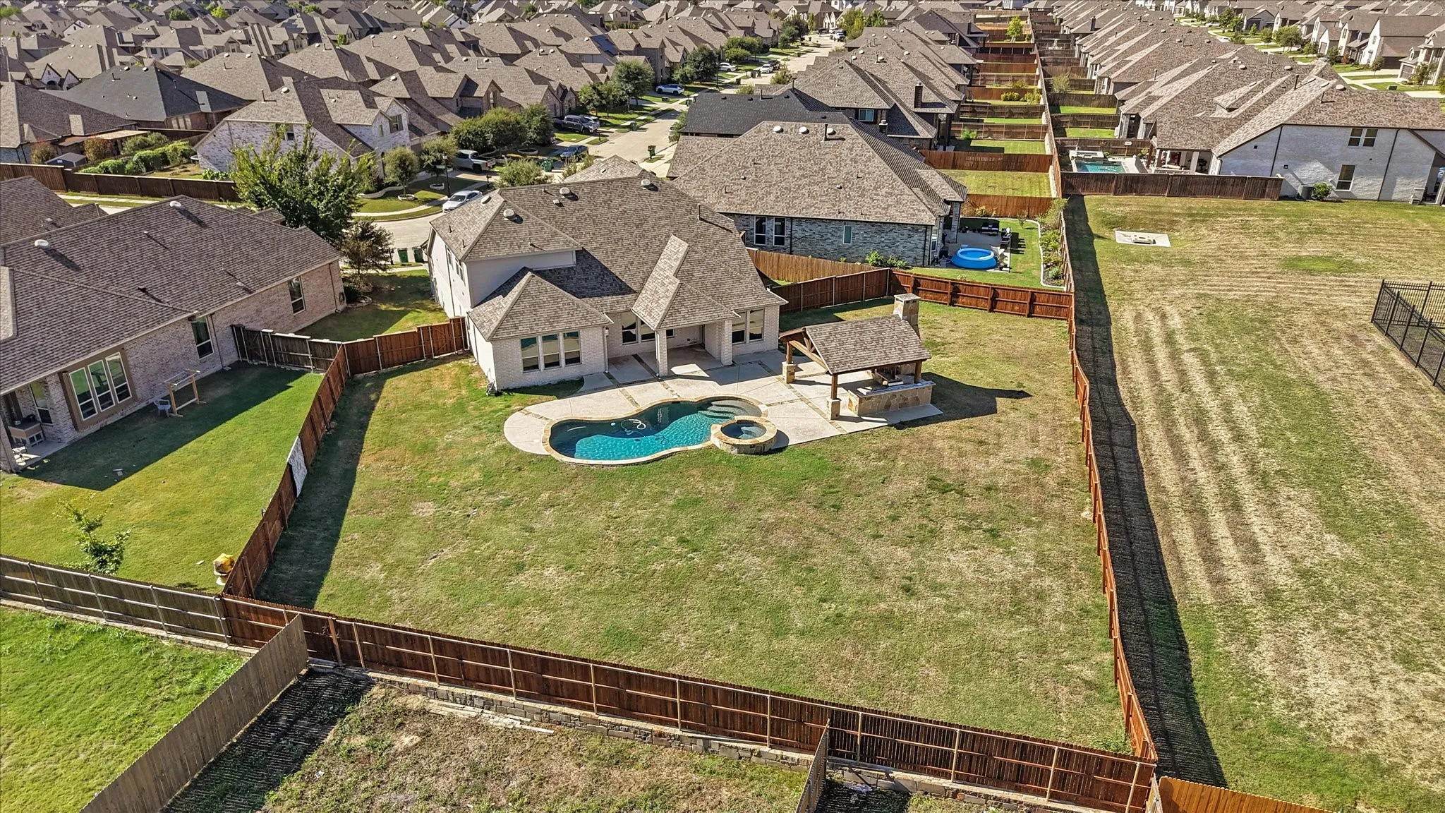 Curved swimming pool, integrated hot tub, covered outdoor kitchen with built-in grill, expansive fenced yard, and stone paver patio