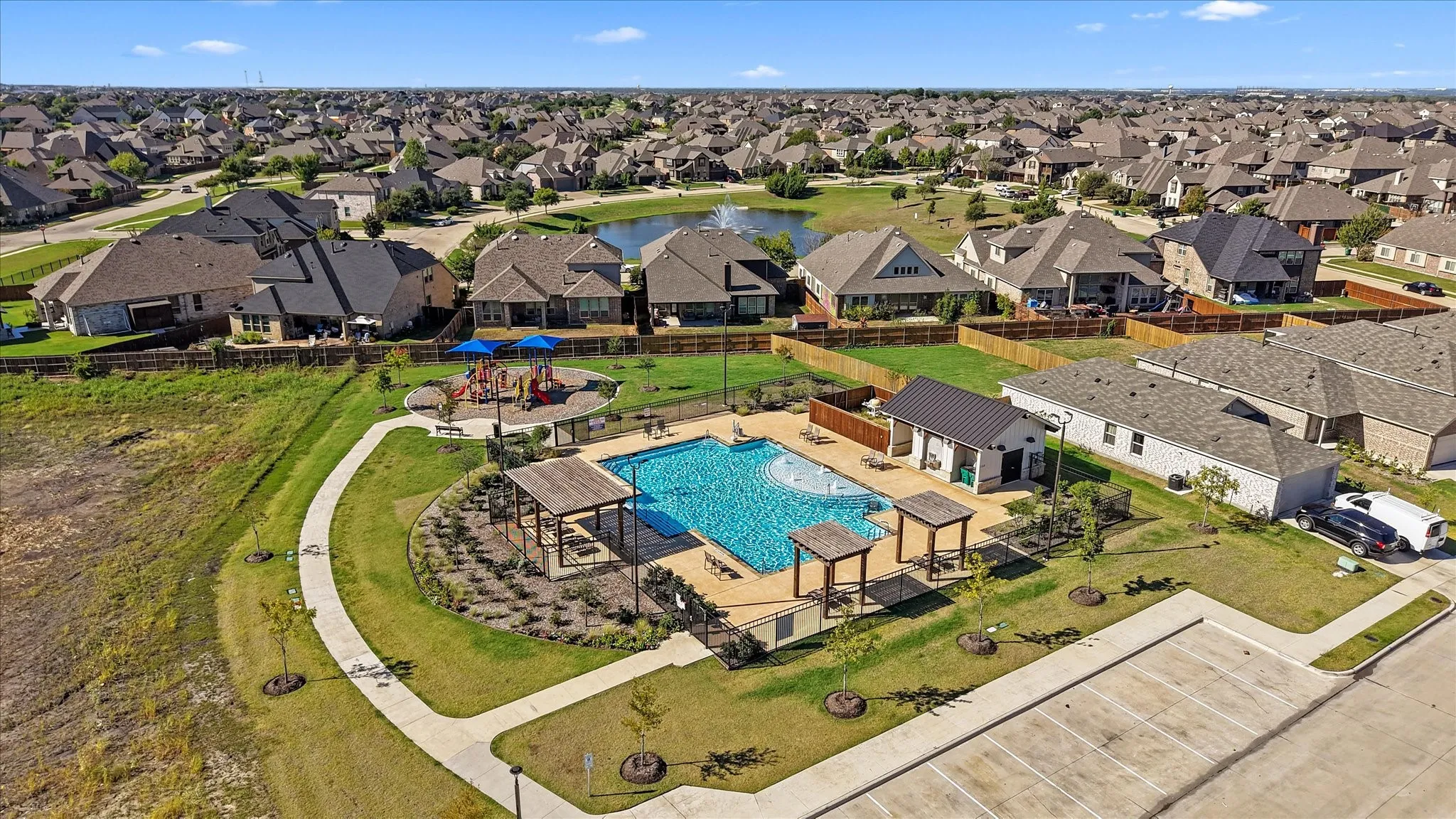 Community pool with integrated splash pad, adjacent playground, surrounding pergolas, and a separate pool house