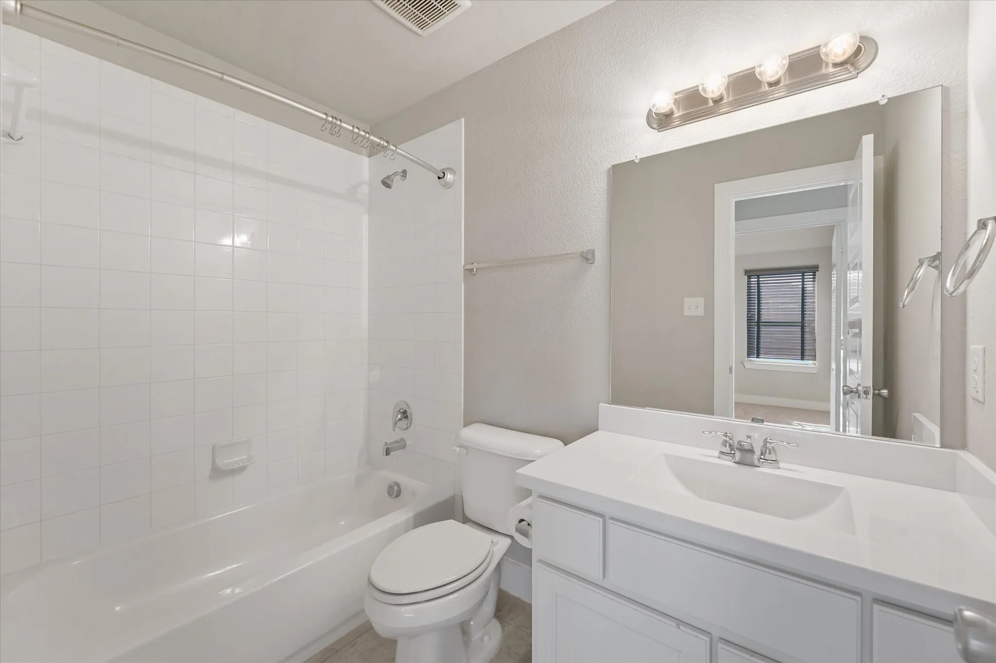 White tile shower surround, shower/tub combination, single vanity with integrated sink, chrome fixtures, and mounted mirror