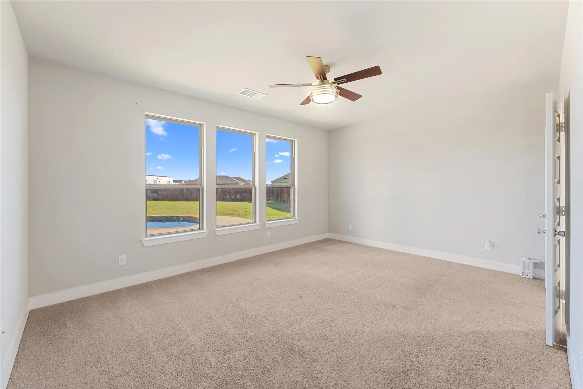 Spacious room featuring three large windows, neutral carpet flooring, a ceiling fan with light, and light-colored walls