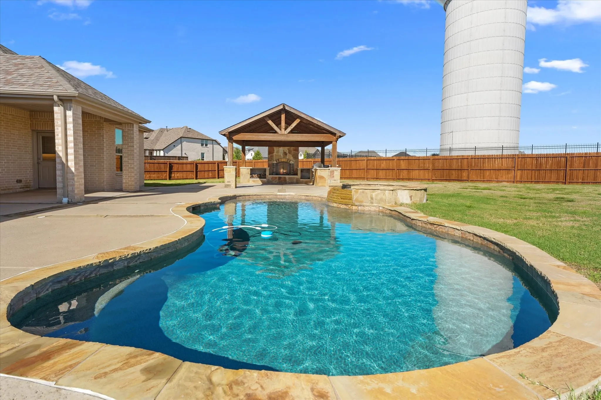 Freeform pool with stone coping, an integrated spa, and an adjacent covered patio featuring a stone fireplace