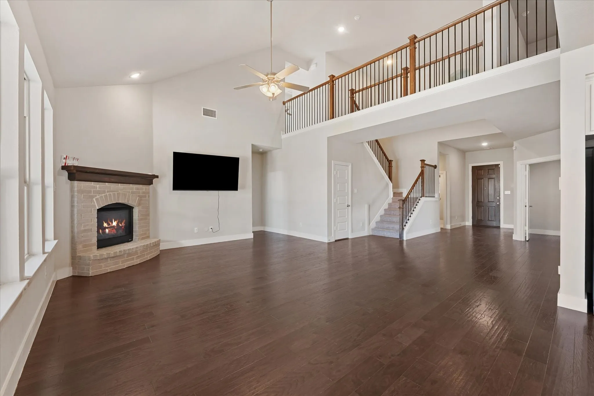 Vaulted ceiling with a ceiling fan, stone fireplace with a wood mantle, wood-finish flooring, and a second-story landing with an open baluster railing