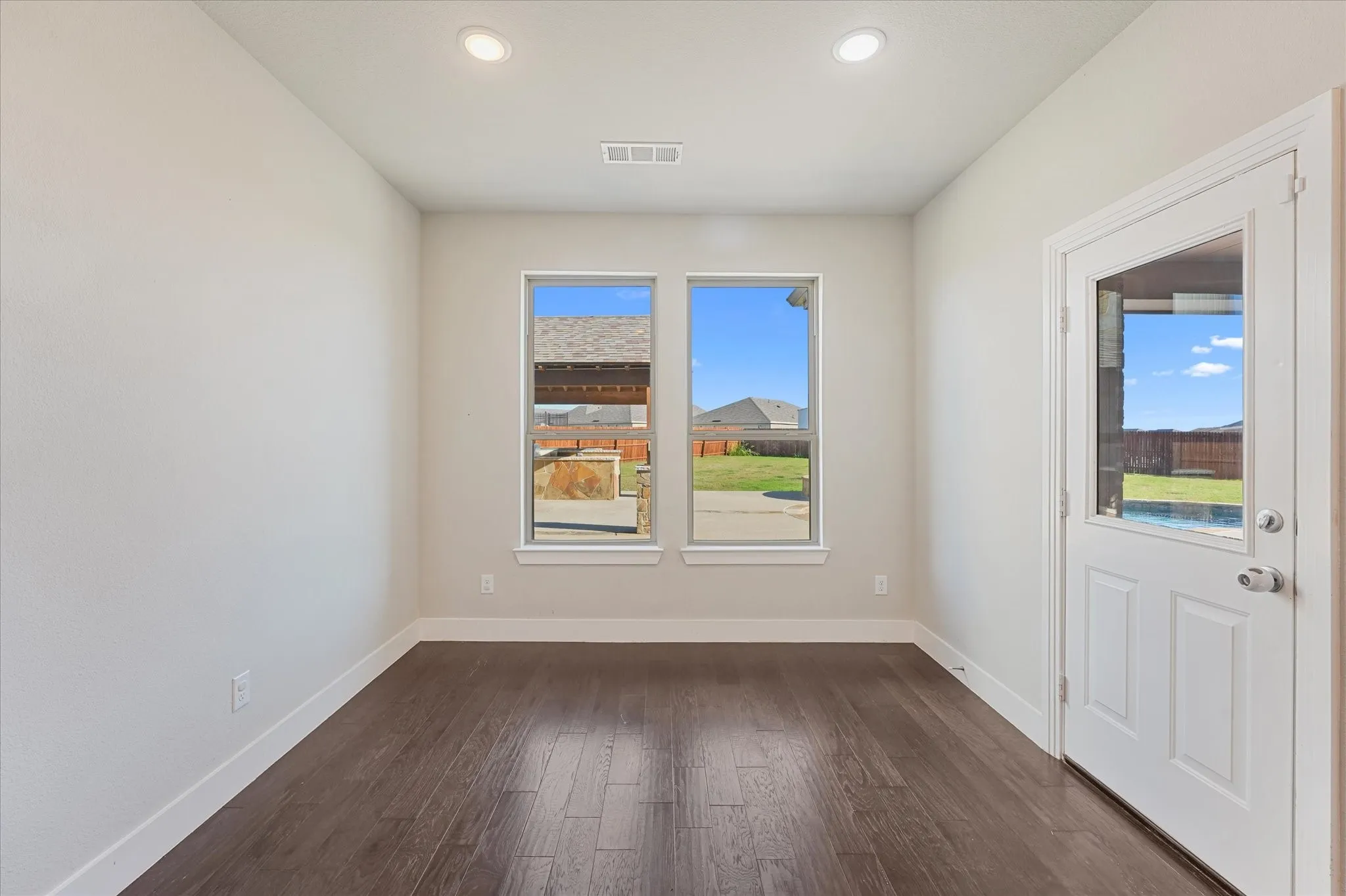 Recessed ceiling lighting, two windows, wood-finish flooring, and a glass-paneled exterior door