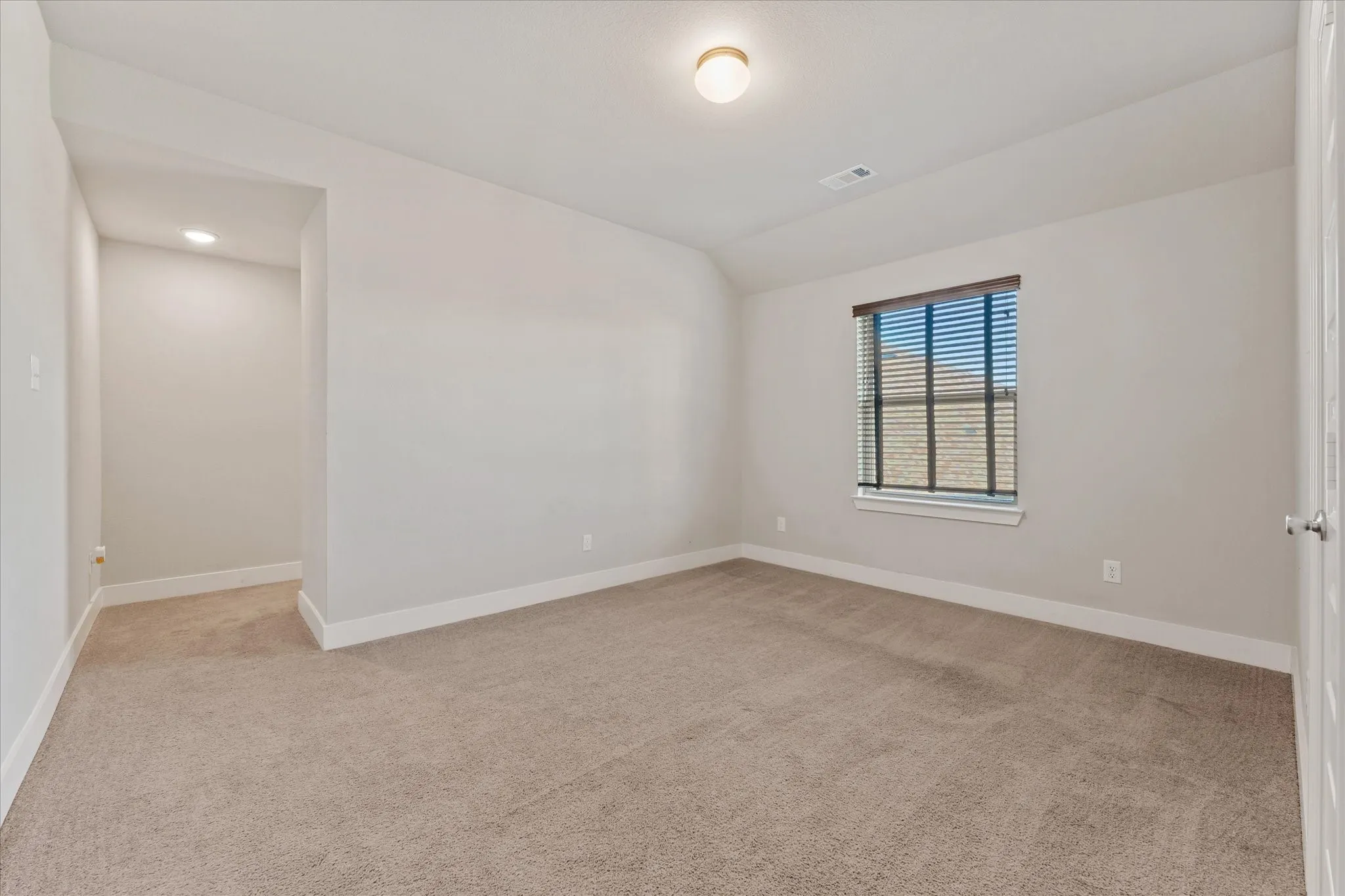 Spacious room featuring neutral carpeting, light-toned walls, and a single window with blinds