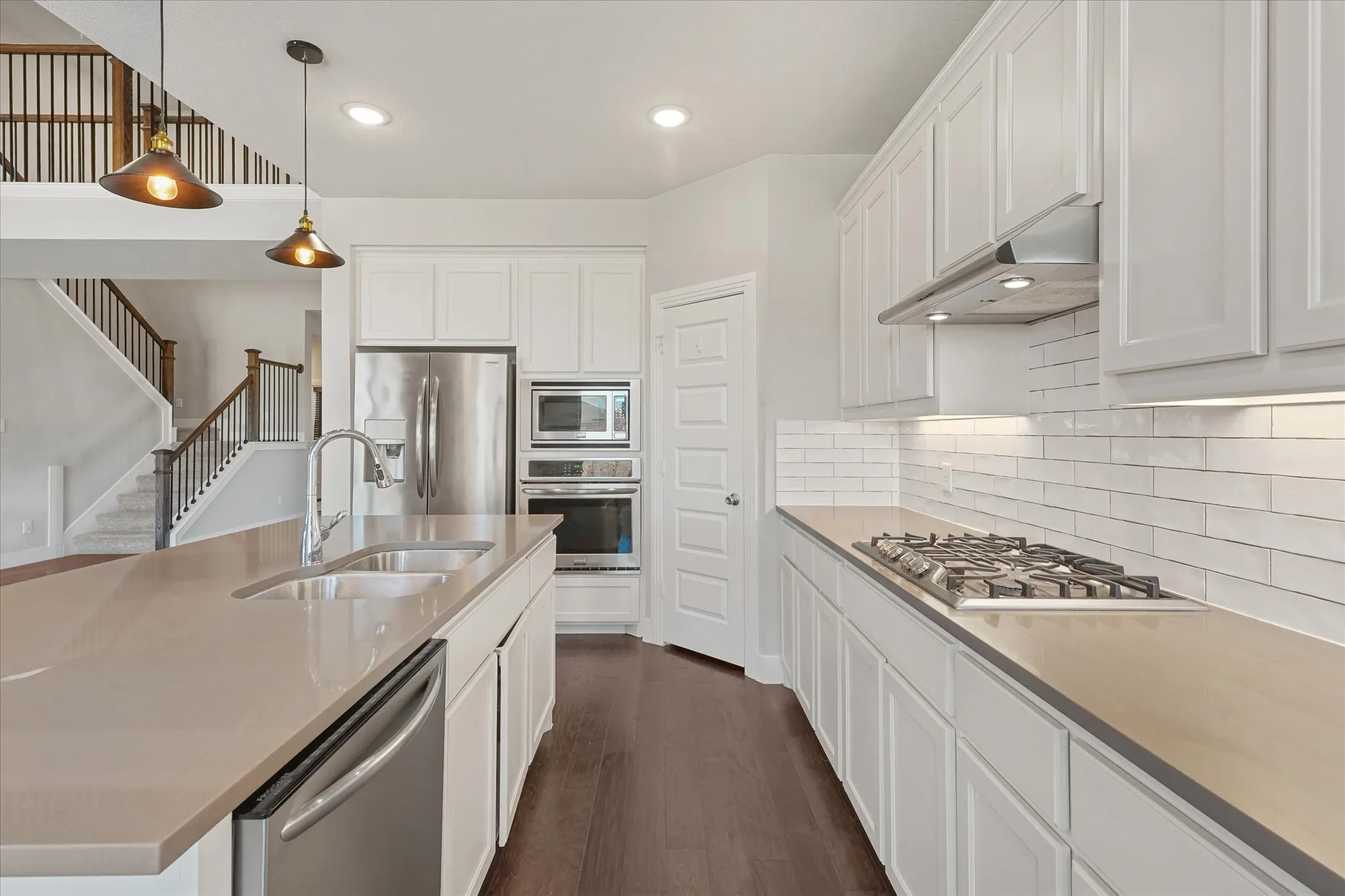 Contemporary kitchen featuring white cabinetry, stainless steel appliances, a center island with double sink, subway tile backsplash, and dark wood-finish flooring