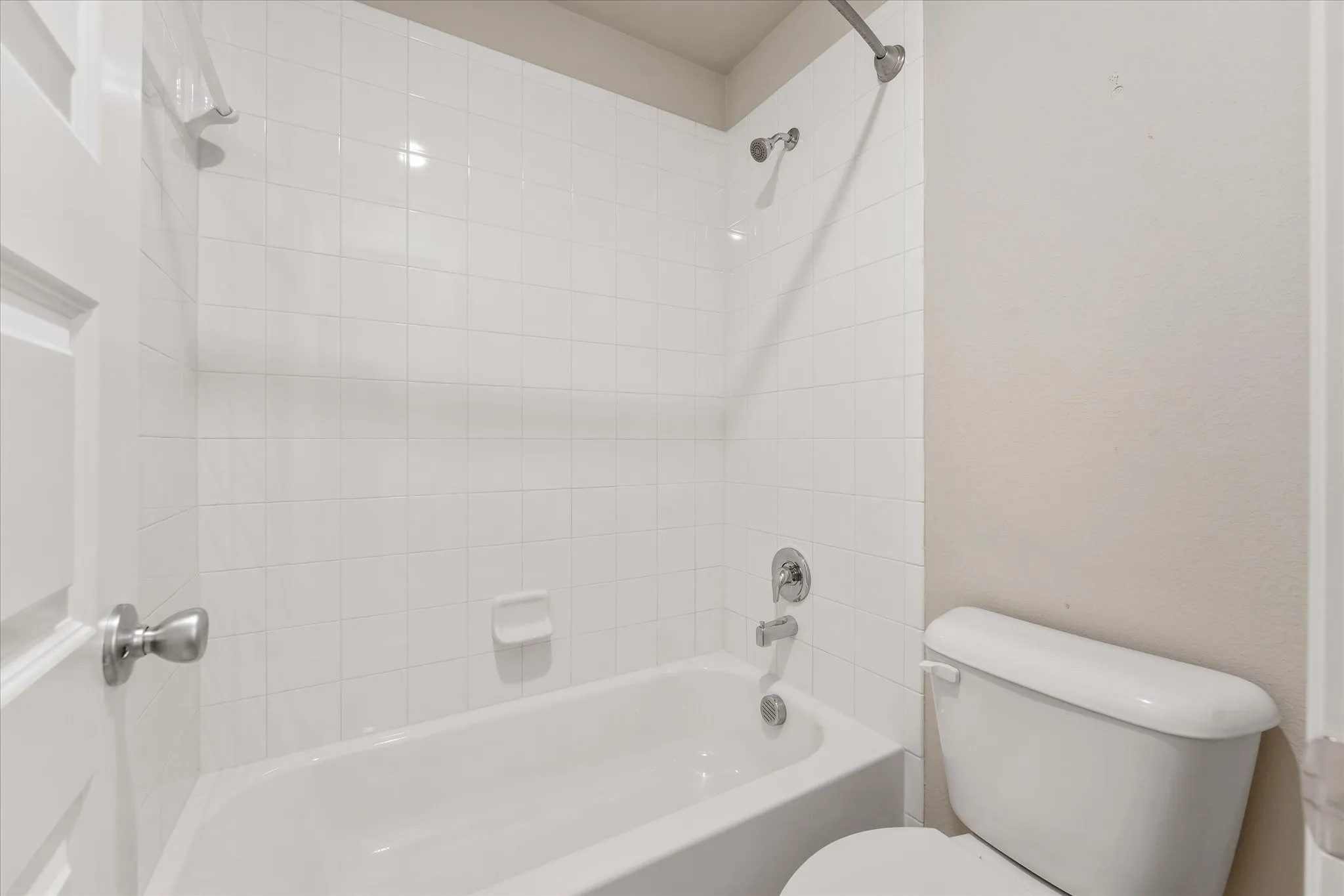 Bathtub with white tile surround, chrome fixtures, and a white toilet