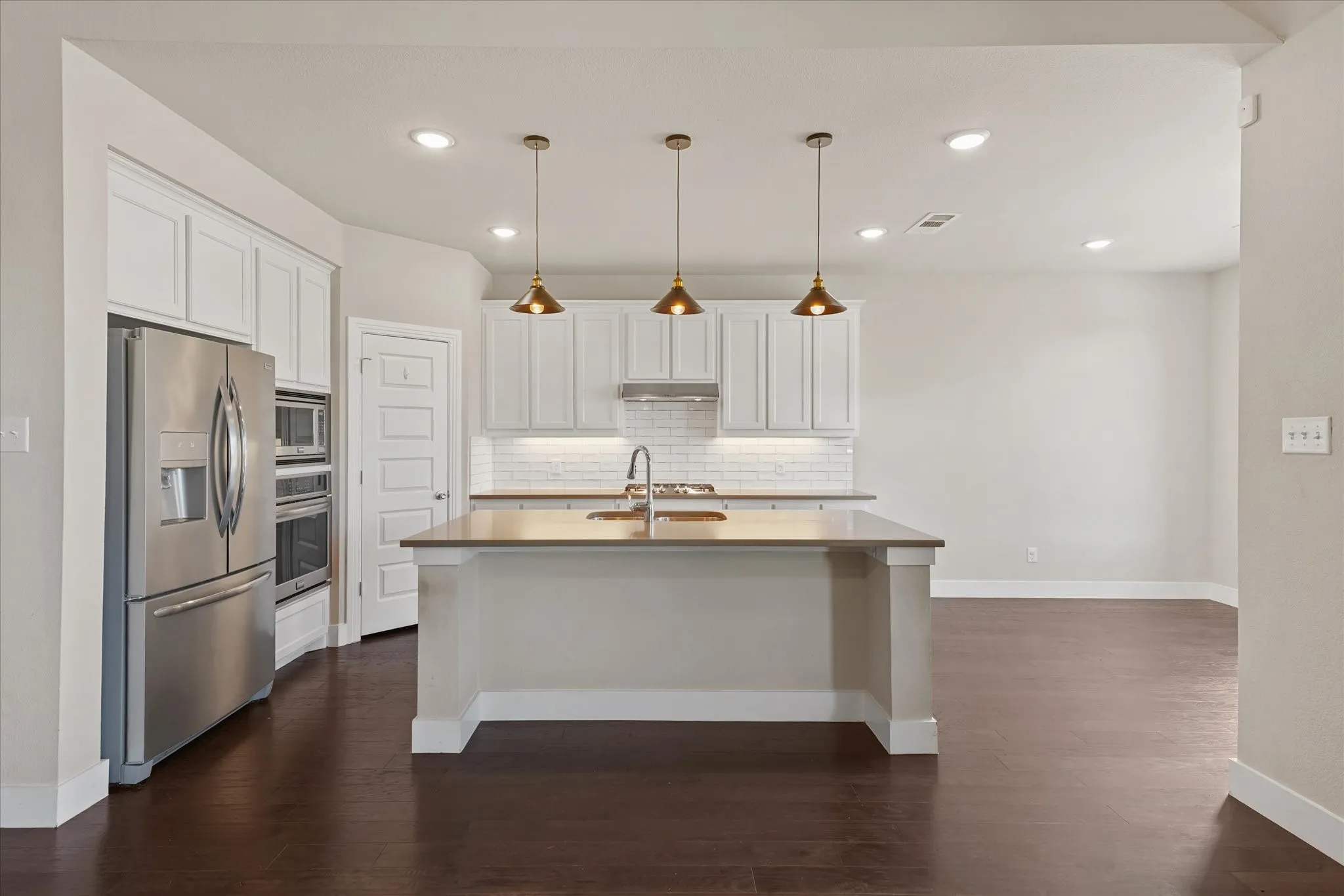 Kitchen featuring white cabinetry, stainless steel appliances, a center island with sink, subway tile backsplash, and dark wood-finish flooring
