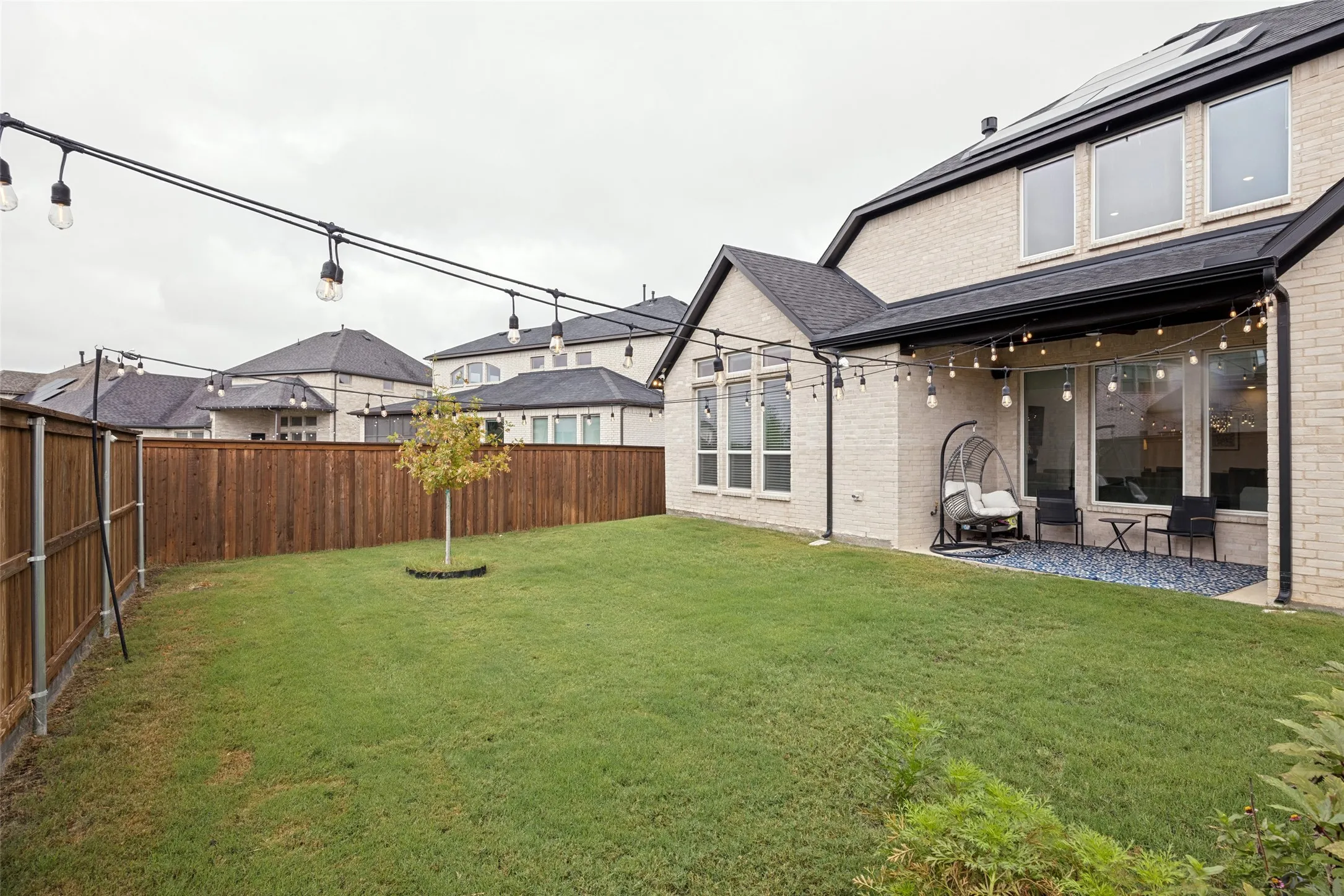 Expansive green lawn, wood privacy fencing, covered patio, string lighting, and brick exterior