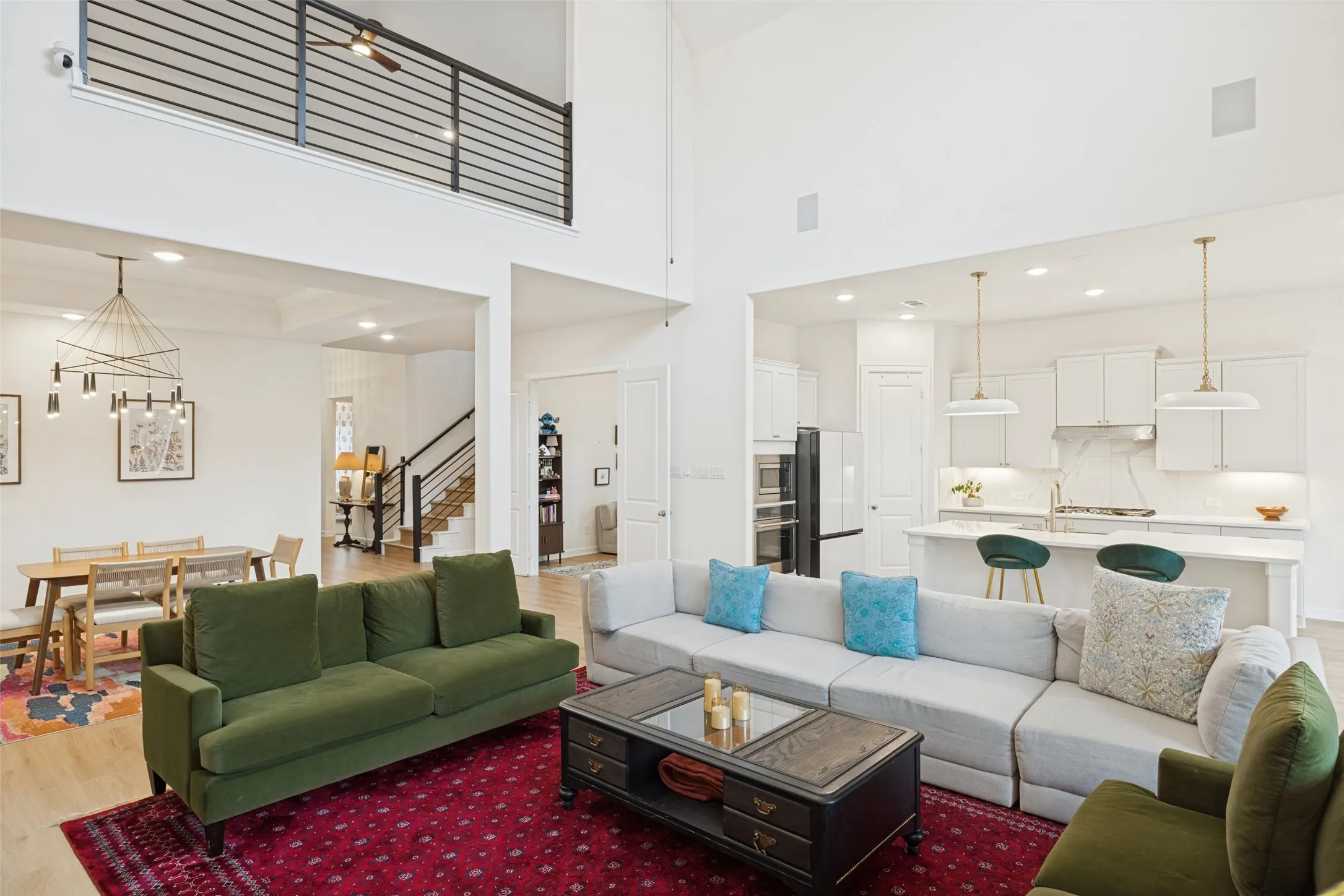 Two-story living area with high ceilings, an upper-level balcony with metal railings, and wood-finish flooring
