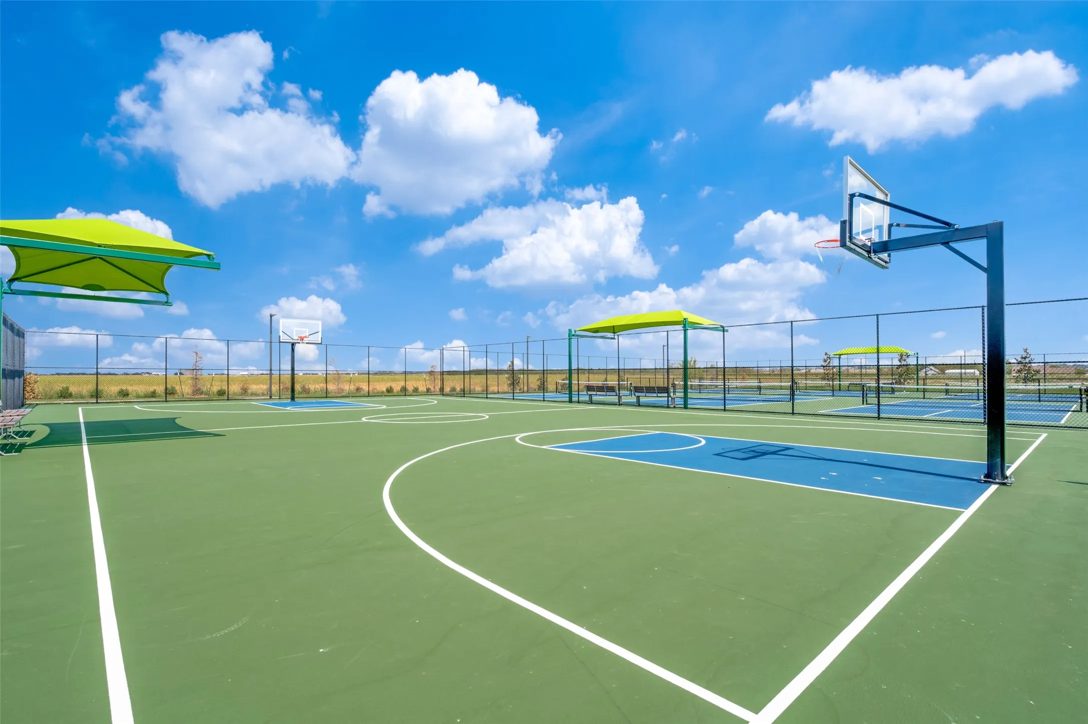 Multi-sport court with green and blue surfacing, multiple basketball hoops, and shaded seating areas