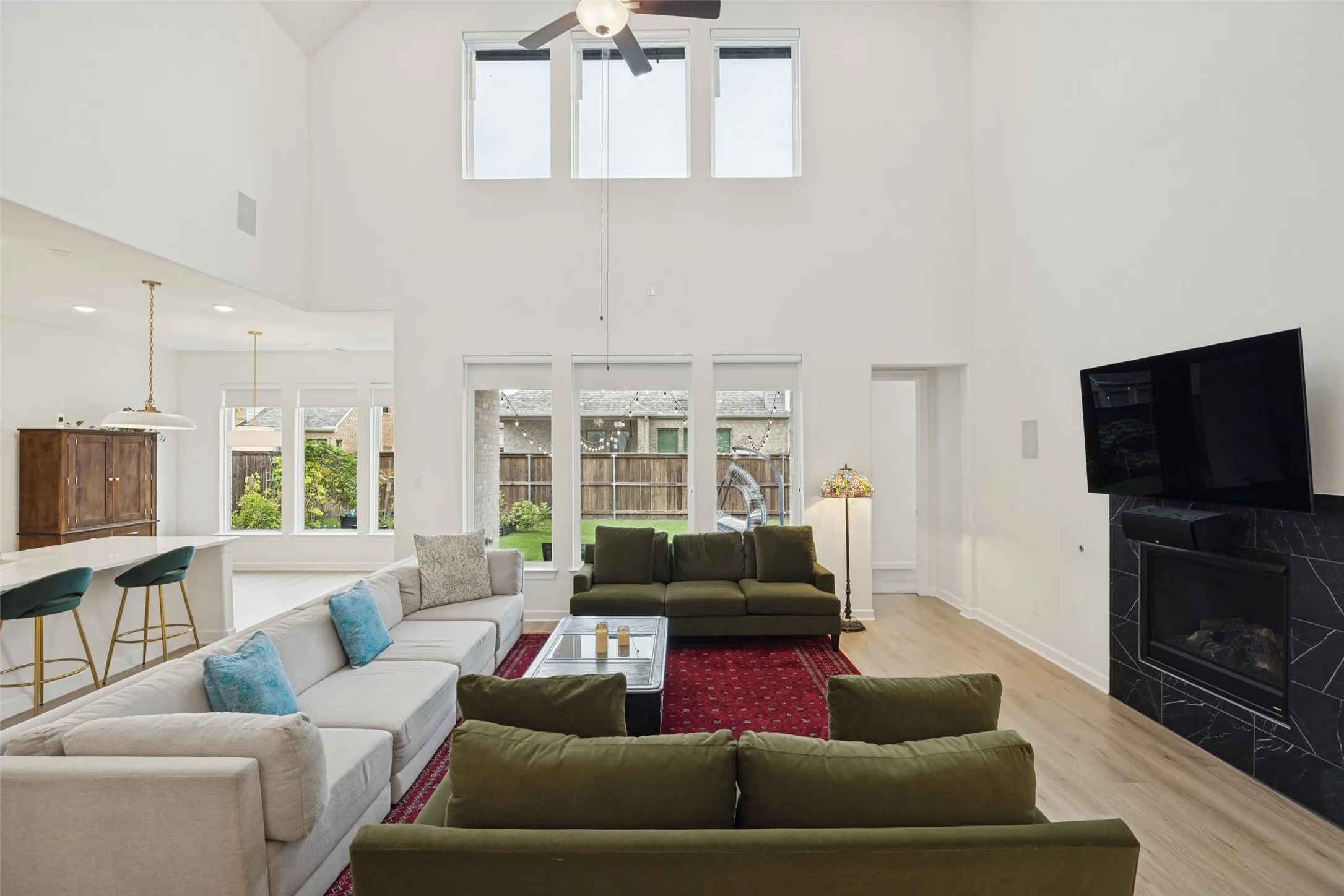 Expansive living area with vaulted ceilings, large windows, wood-finish flooring, and a built-in fireplace with a dark stone surround