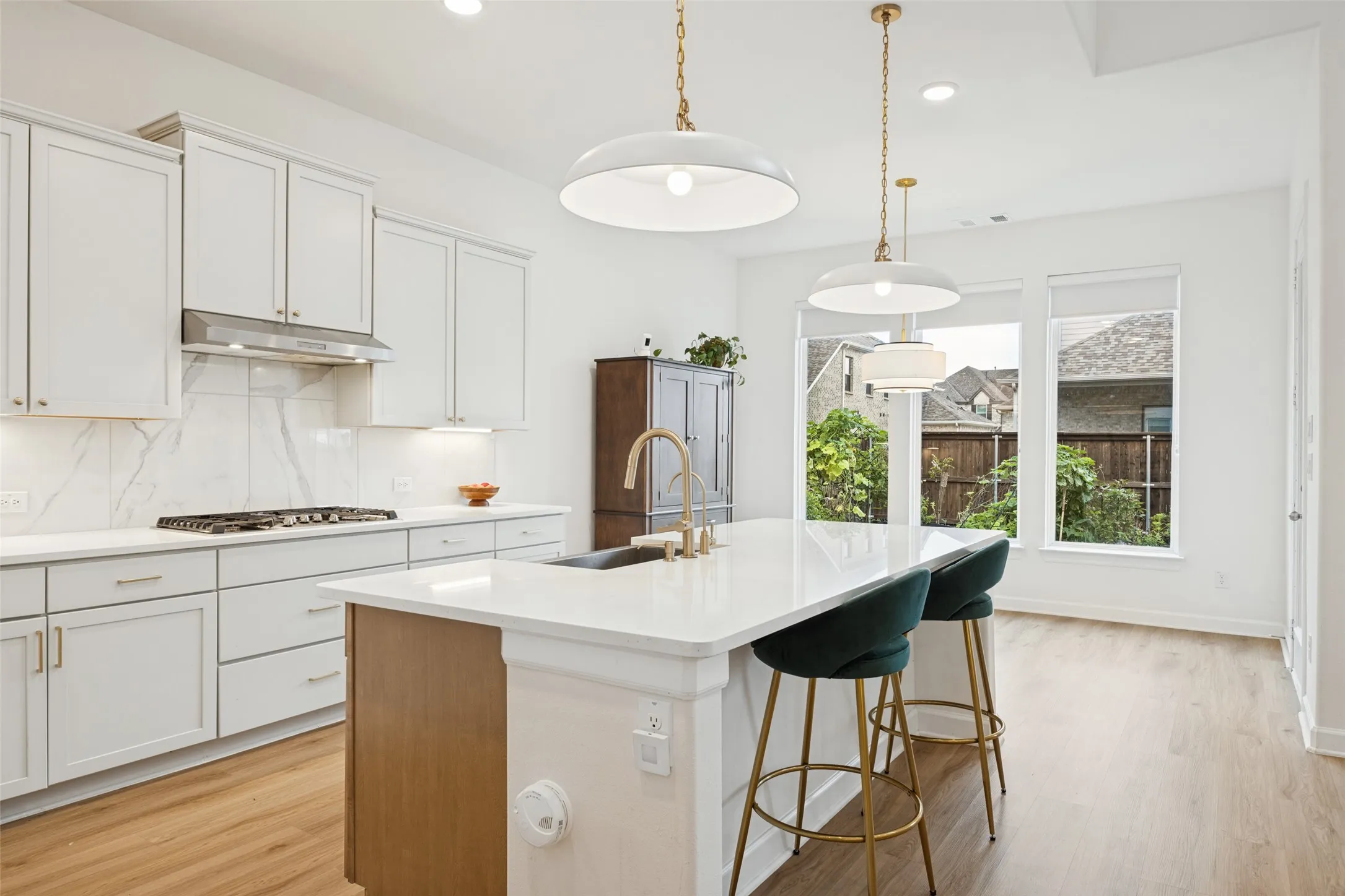 Open-concept kitchen featuring white cabinetry, a gas cooktop with stainless steel hood, an island with countertop seating, white countertops with a veined backsplash, and wood-finish flooring