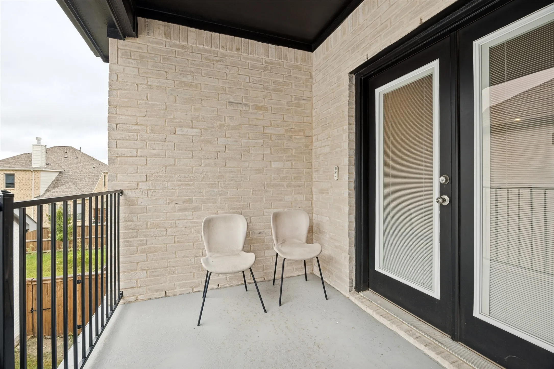 Private balcony featuring a light-colored brick exterior, black iron railing, and dark-framed double doors with obscured glass panels