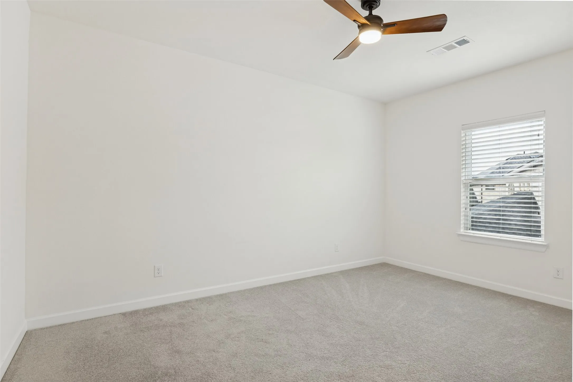 Neutral painted walls, gray carpet, and a window with blinds, complemented by a ceiling fan with integrated lighting