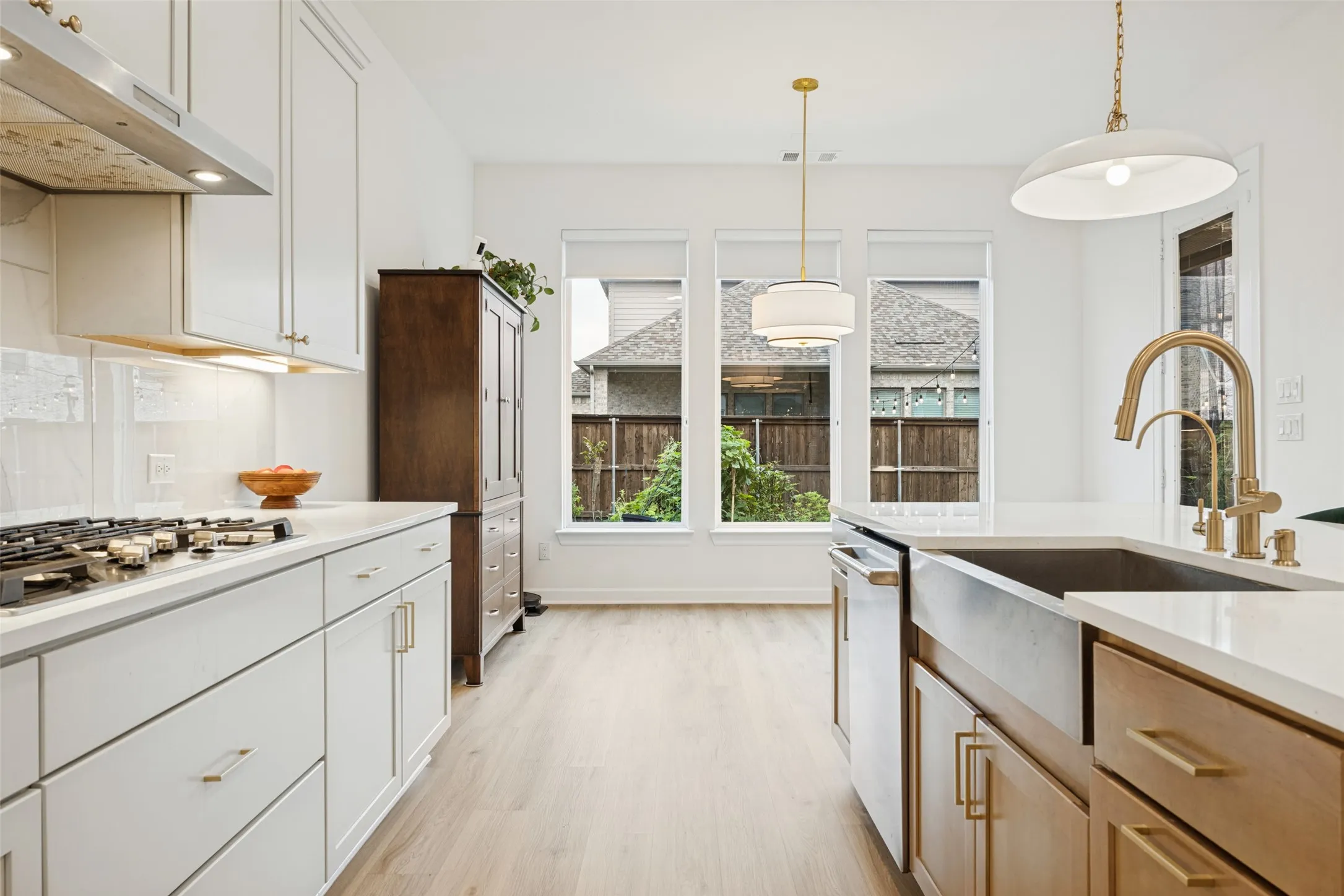 Contemporary kitchen featuring white cabinetry, a gas range with a stainless steel hood, quartz countertops, a farmhouse sink with a gold-tone faucet, and wood-finish flooring