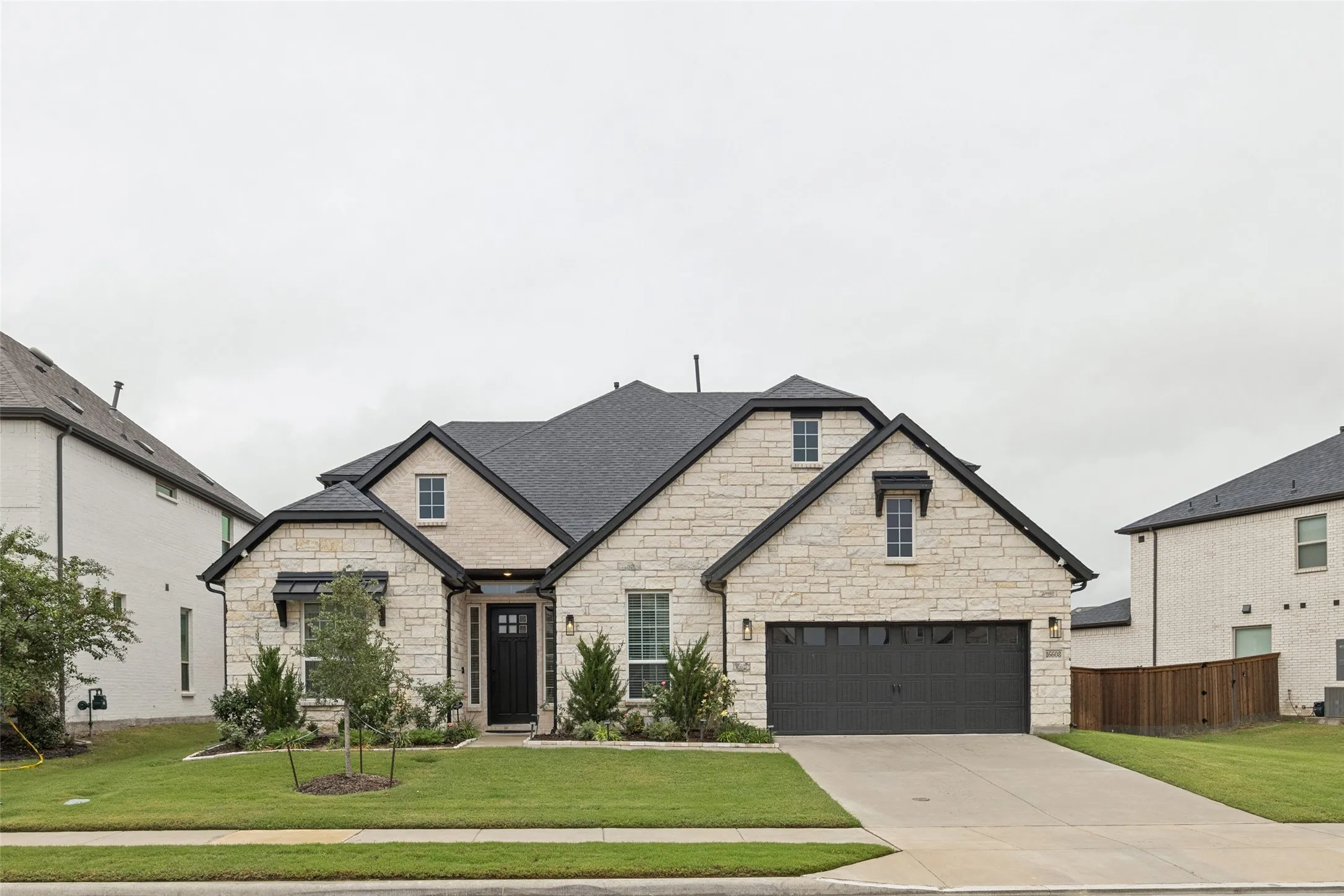 Stone facade with dark trim, dark shingle roof, and a two-car garage