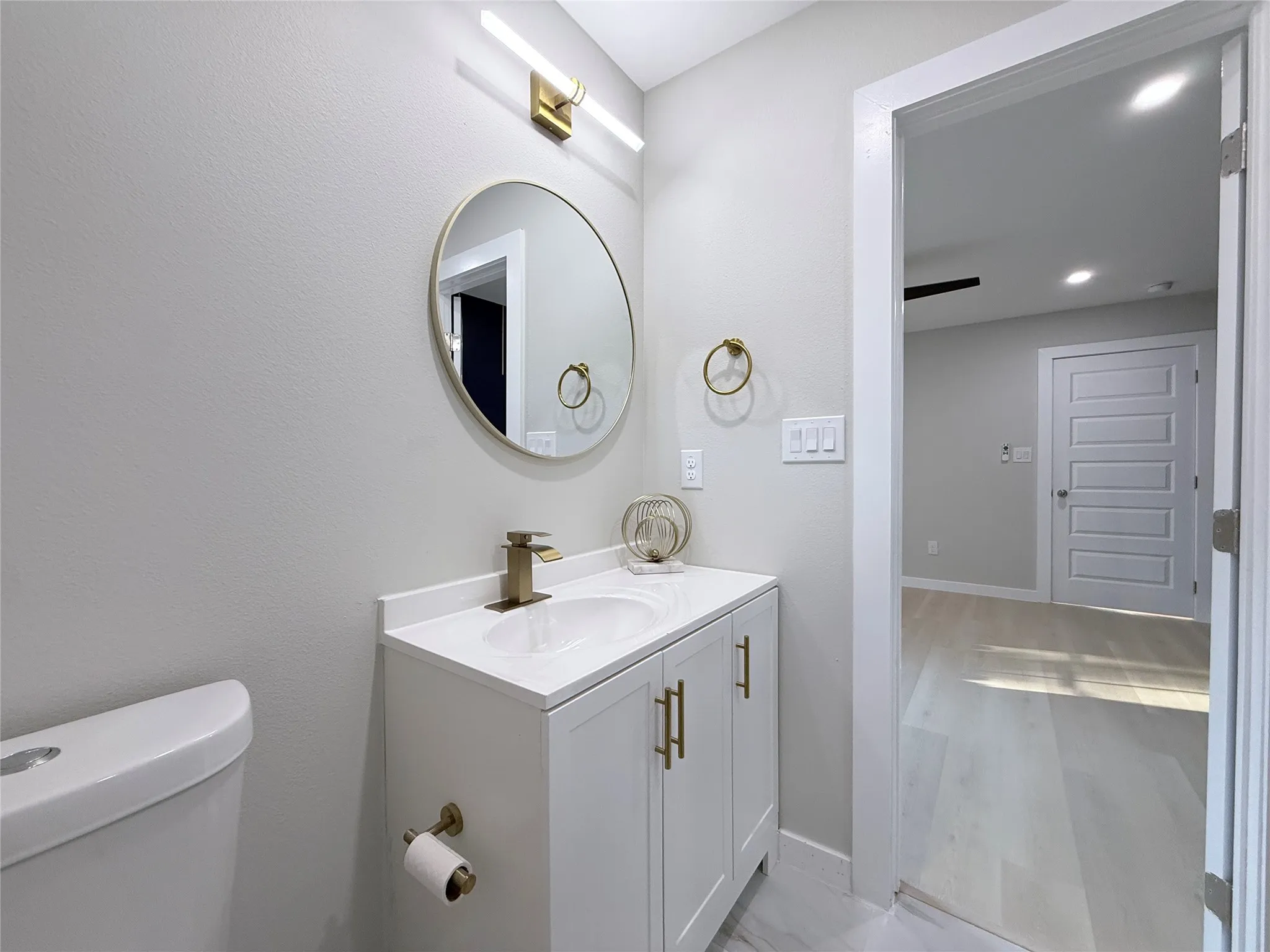 White vanity with gold-finish hardware, a circular mirror, and a gold-finish faucet