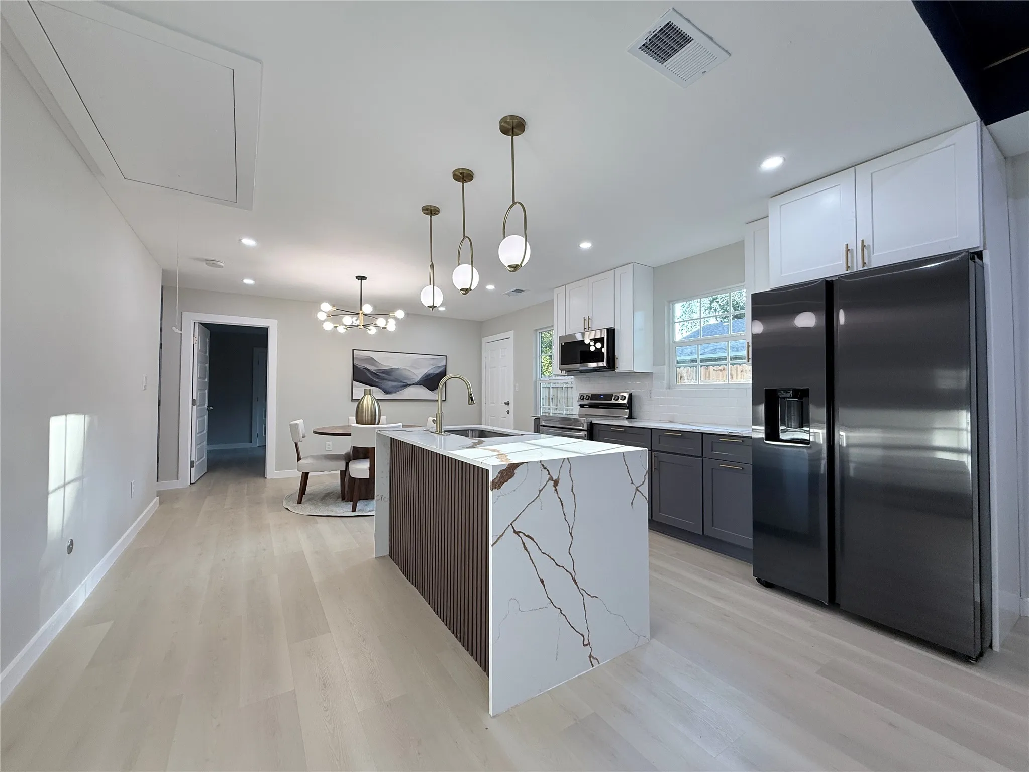 Modern kitchen featuring an island with a waterfall countertop, contemporary pendant lighting, light wood-finish flooring, white upper cabinetry, and dark lower cabinetry