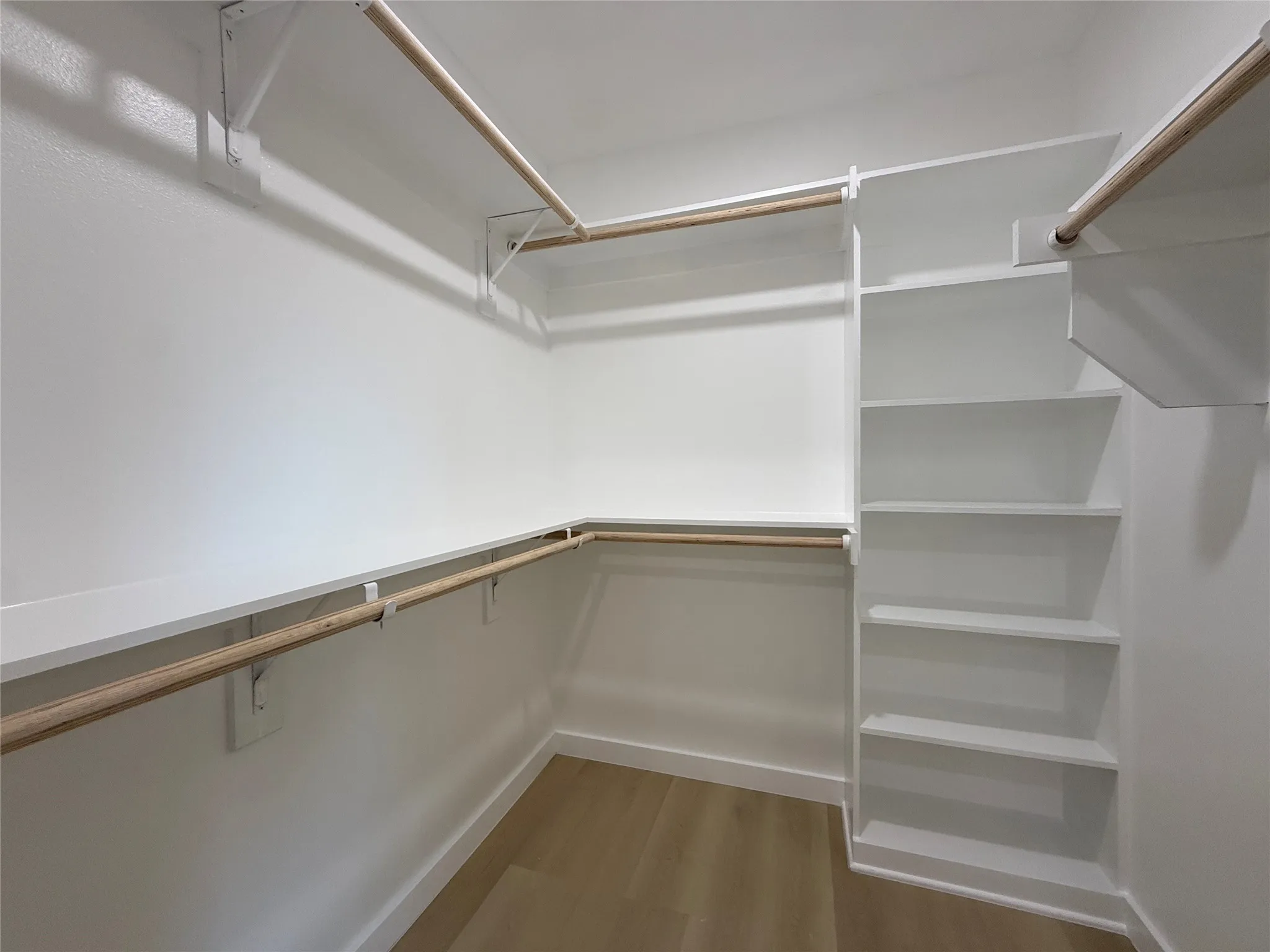 Walk-in closet with multiple hanging rods, built-in shelving, and wood-finish flooring