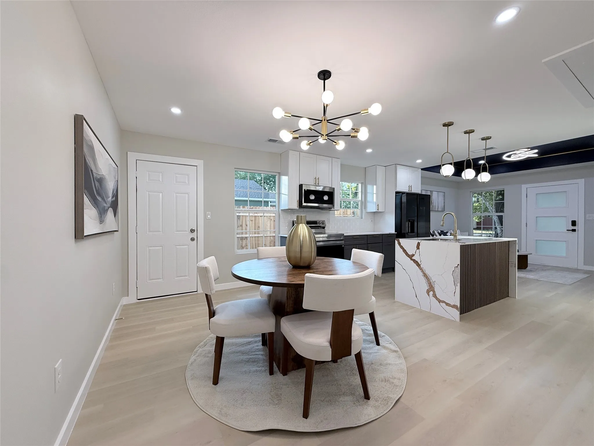 Open-concept living space featuring wood-finish flooring, a modern kitchen island with an integrated sink, and contemporary light fixtures
