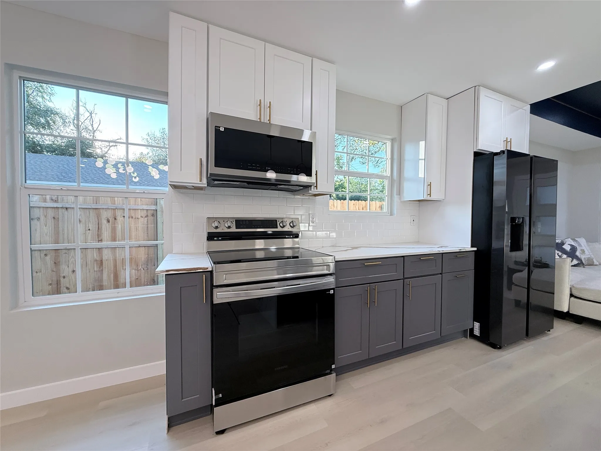Kitchen featuring two-tone cabinetry, stainless steel appliances, white subway tile backsplash, light wood-finish flooring, and white countertops