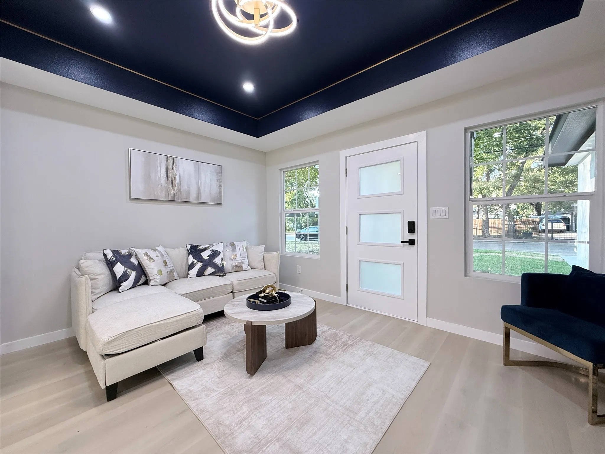 Recessed ceiling with an accent color, contemporary chandelier, white walls, light wood-finish flooring, and a modern entry door with frosted panels