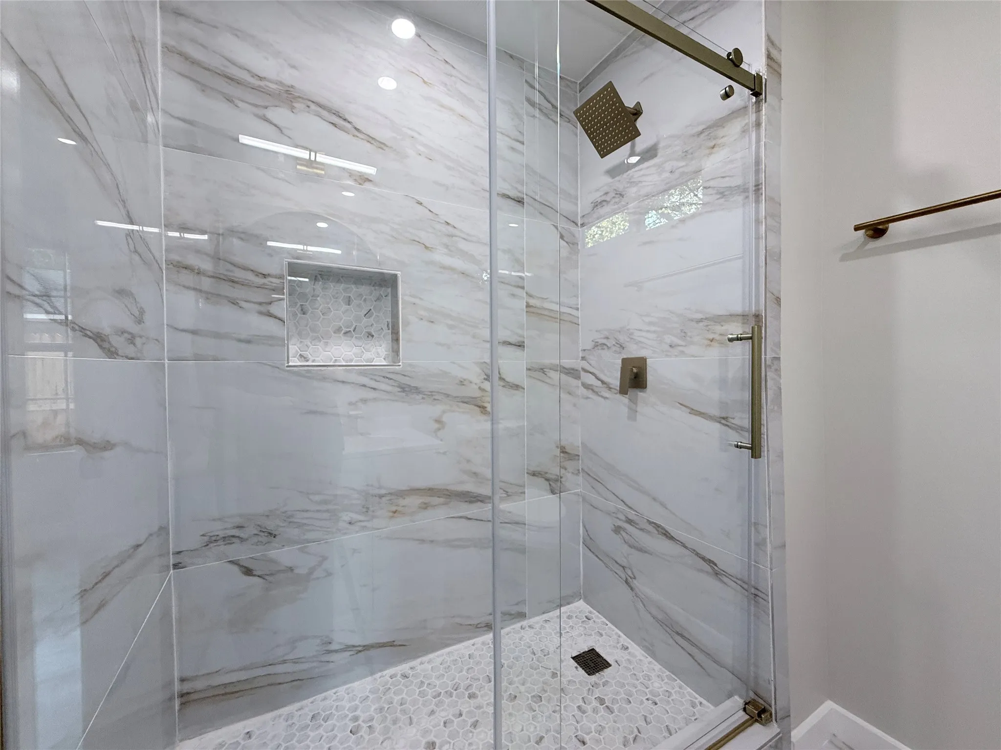 Glass-enclosed shower with large format marble-look tile walls, a built-in niche with mosaic tile, and a pebble-tile shower floor