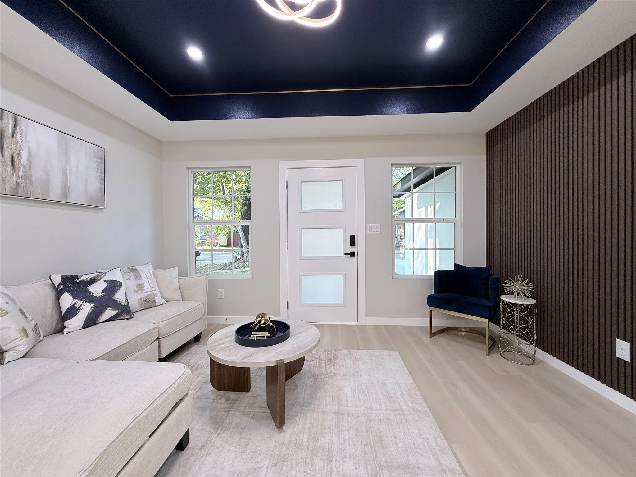 Tray ceiling with recessed lighting and a central fixture, wood-finish flooring, white paneled door with frosted glass inserts, and a textured accent wall