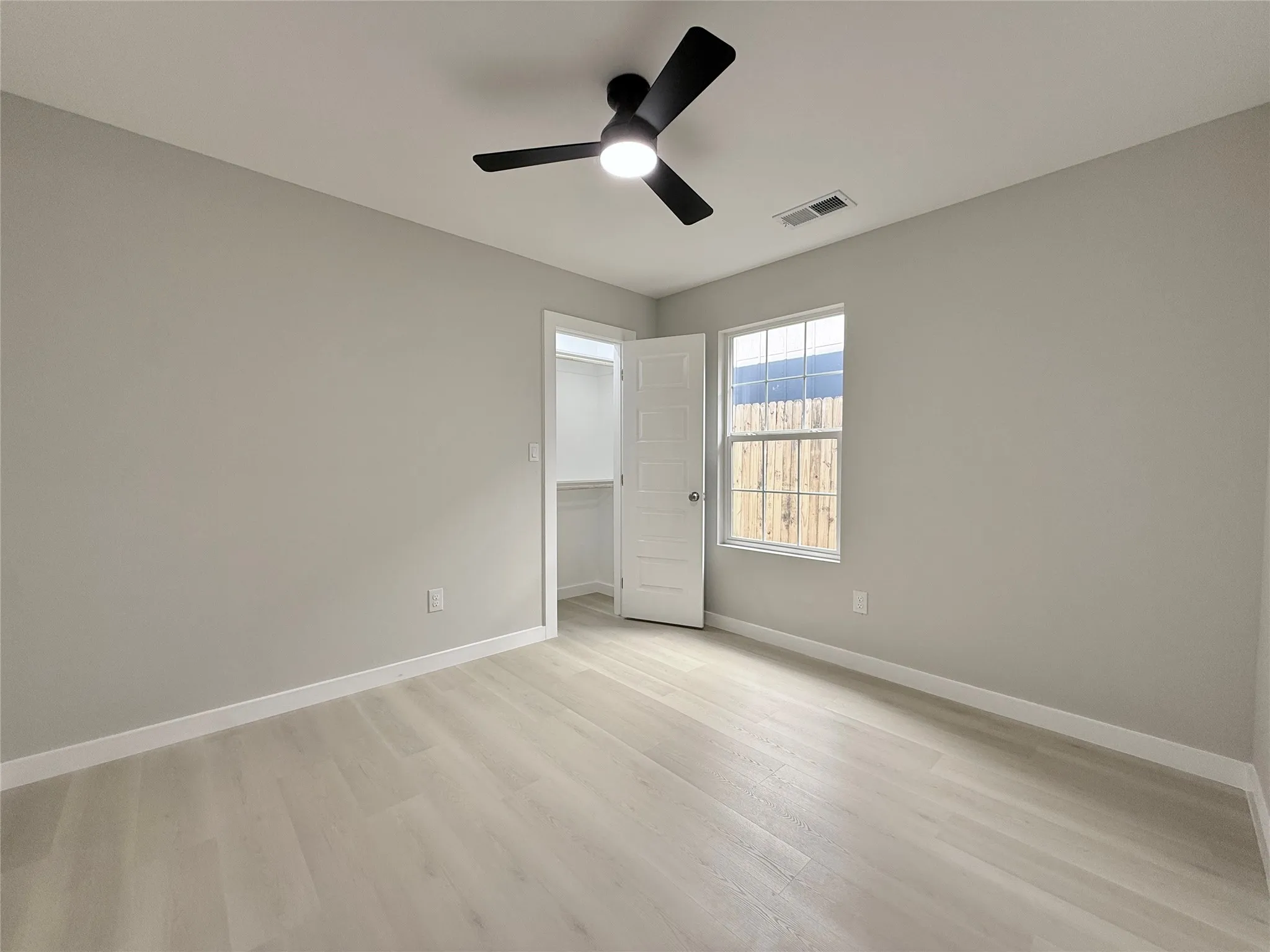 Light wood-finish flooring, a contemporary ceiling fan with integrated lighting, and a window providing natural illumination