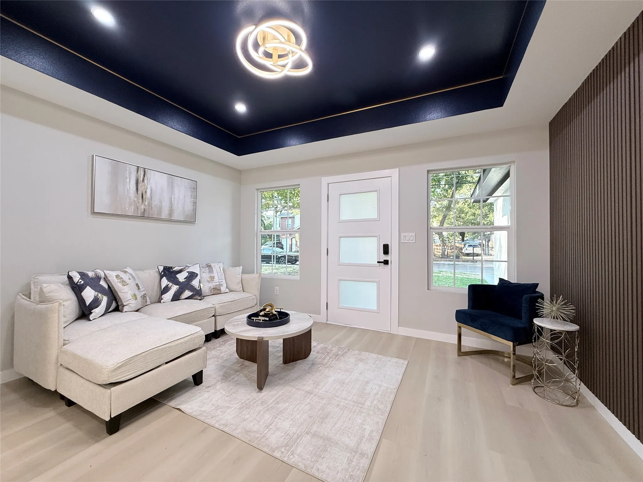 Recessed ceiling with a dark accent color, contemporary chandelier, wood-finish flooring, white entry door with frosted panels, and a textured accent wall