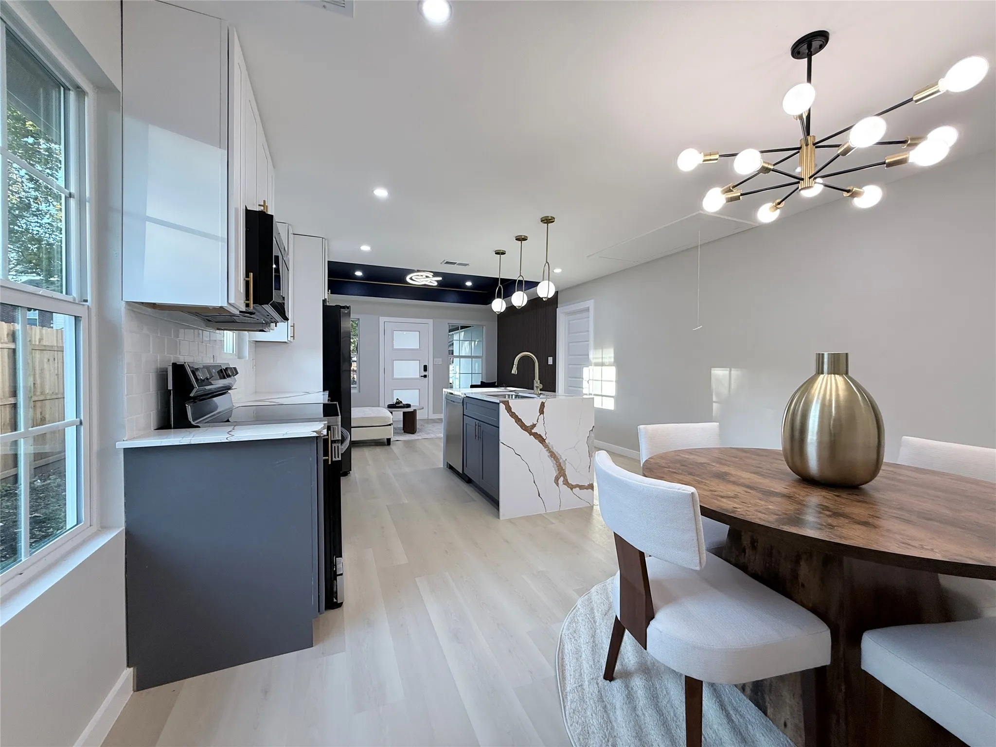 Open-concept living area with light wood-finish flooring, a contemporary chandelier, and a kitchen island featuring a waterfall-edge countertop