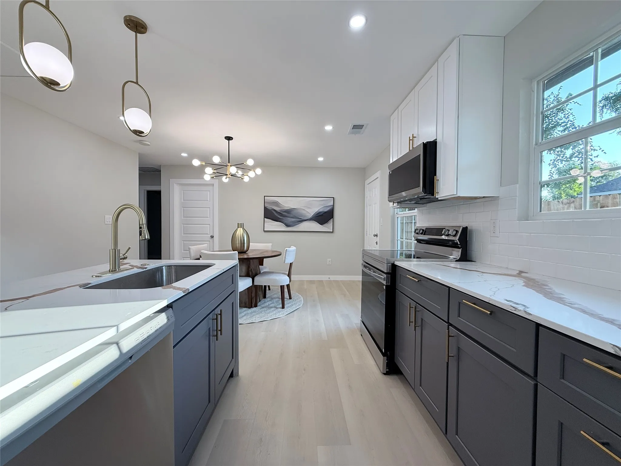 Contemporary kitchen featuring light wood-finish flooring, white subway tile backsplash, and two-tone cabinetry with gold-tone hardware