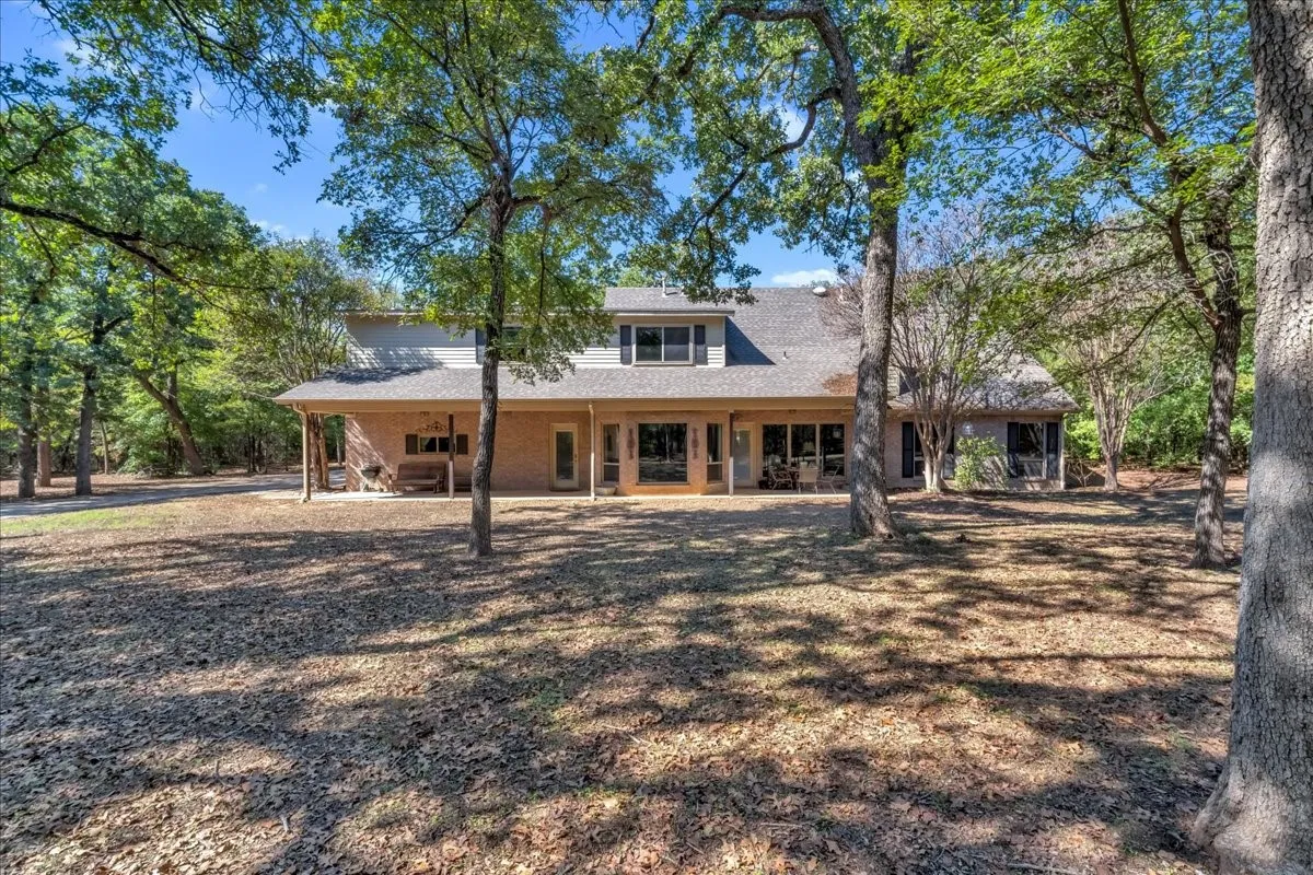 Two-story residence featuring a two-car garage, brick and siding exterior, covered porch, and mature trees