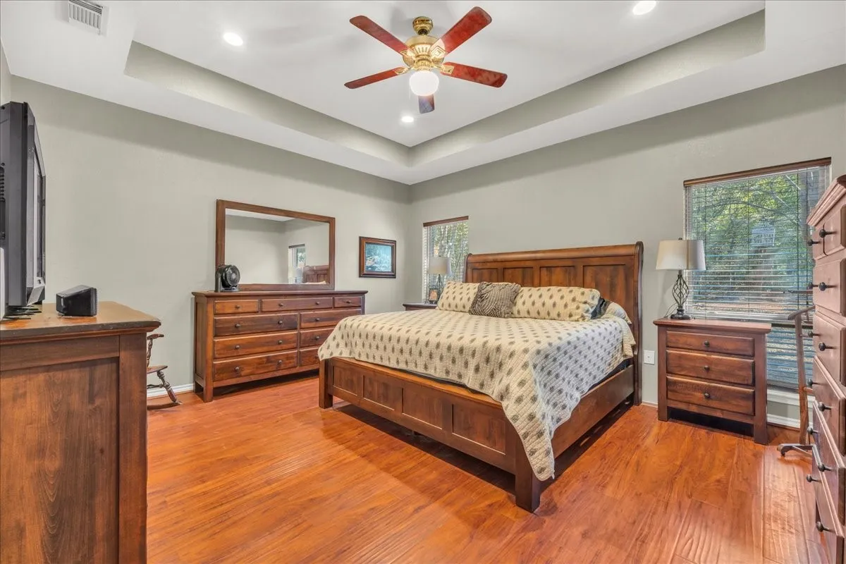 Tray ceiling with recessed lighting and a ceiling fan, wood-finish flooring, and two windows