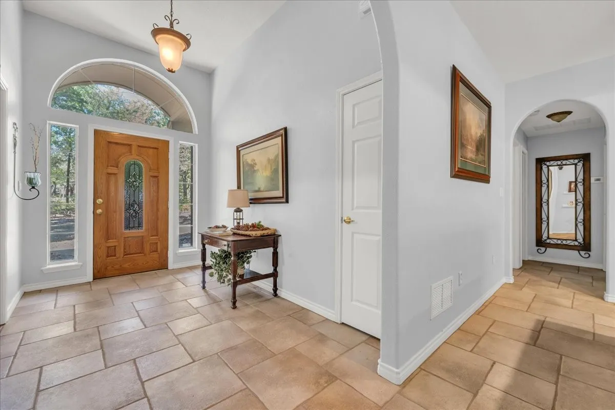 Foyer featuring an arched transom window, solid wood entry door with decorative glass, side light windows, and large format tile flooring